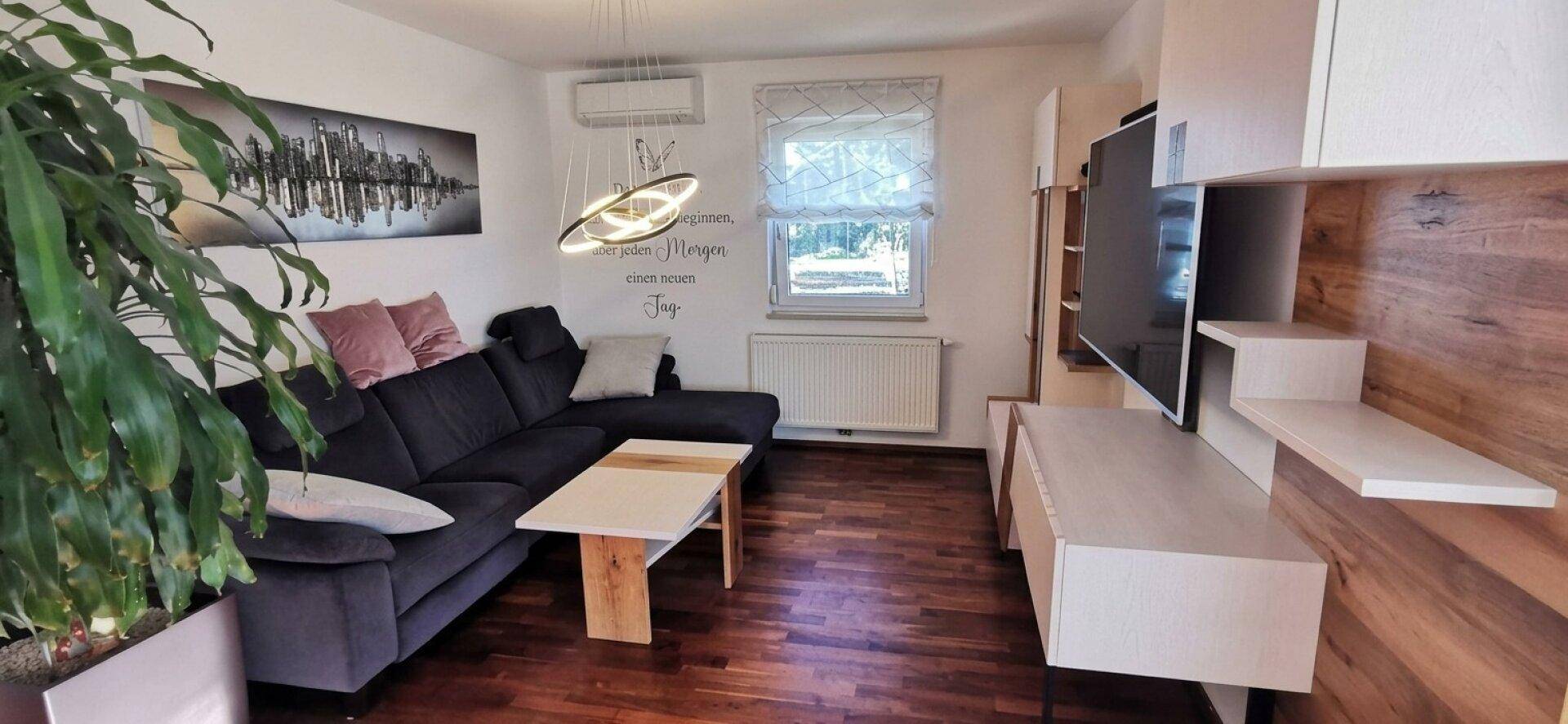 Gemütliches Wohnzimmer mit dunklem Sofa, Holzboden und modernem TV-Möbel.