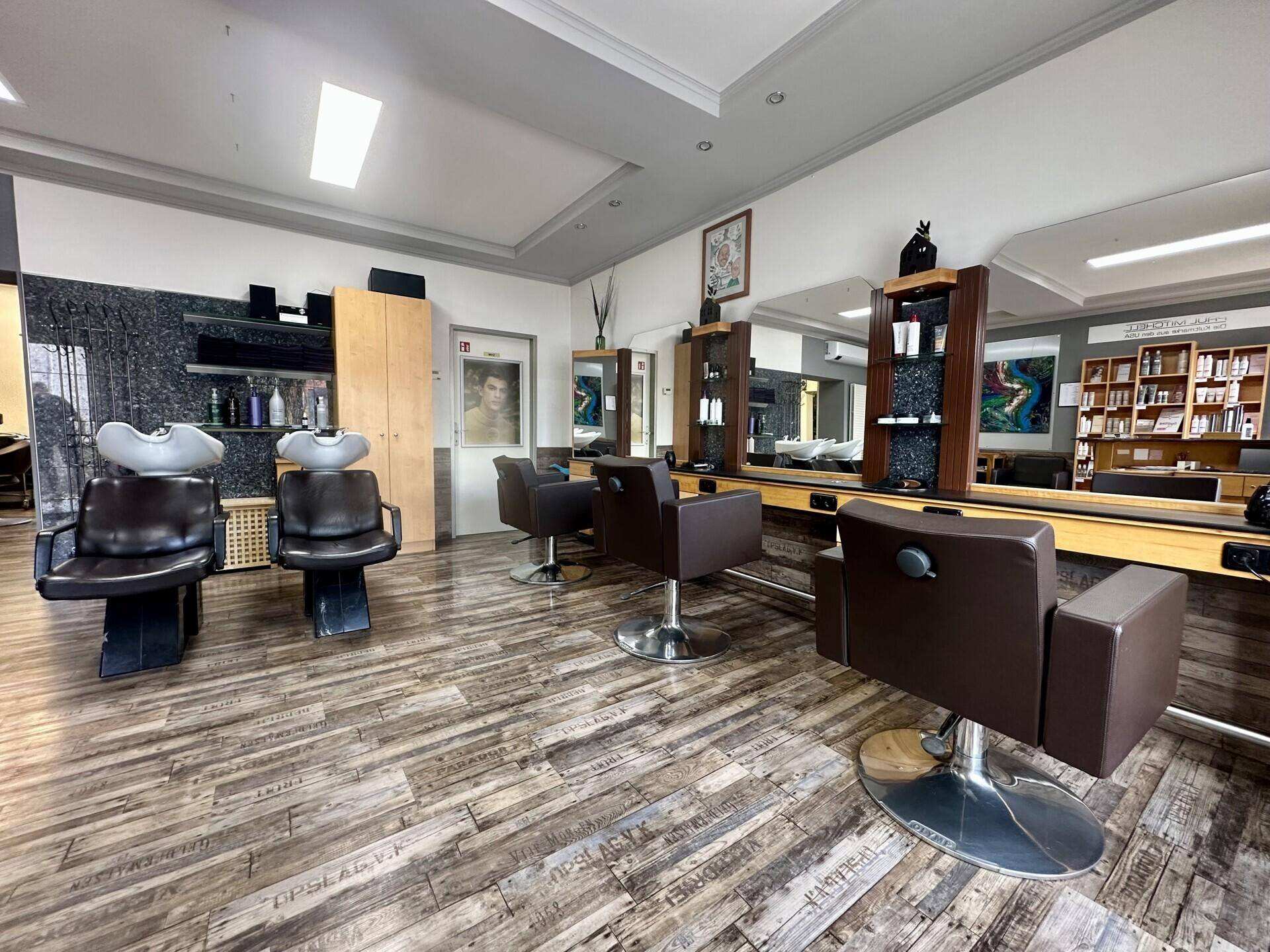 Innenansicht eines Friseursalons mit Stylingstühlen, großen Spiegeln und Holzregalen.