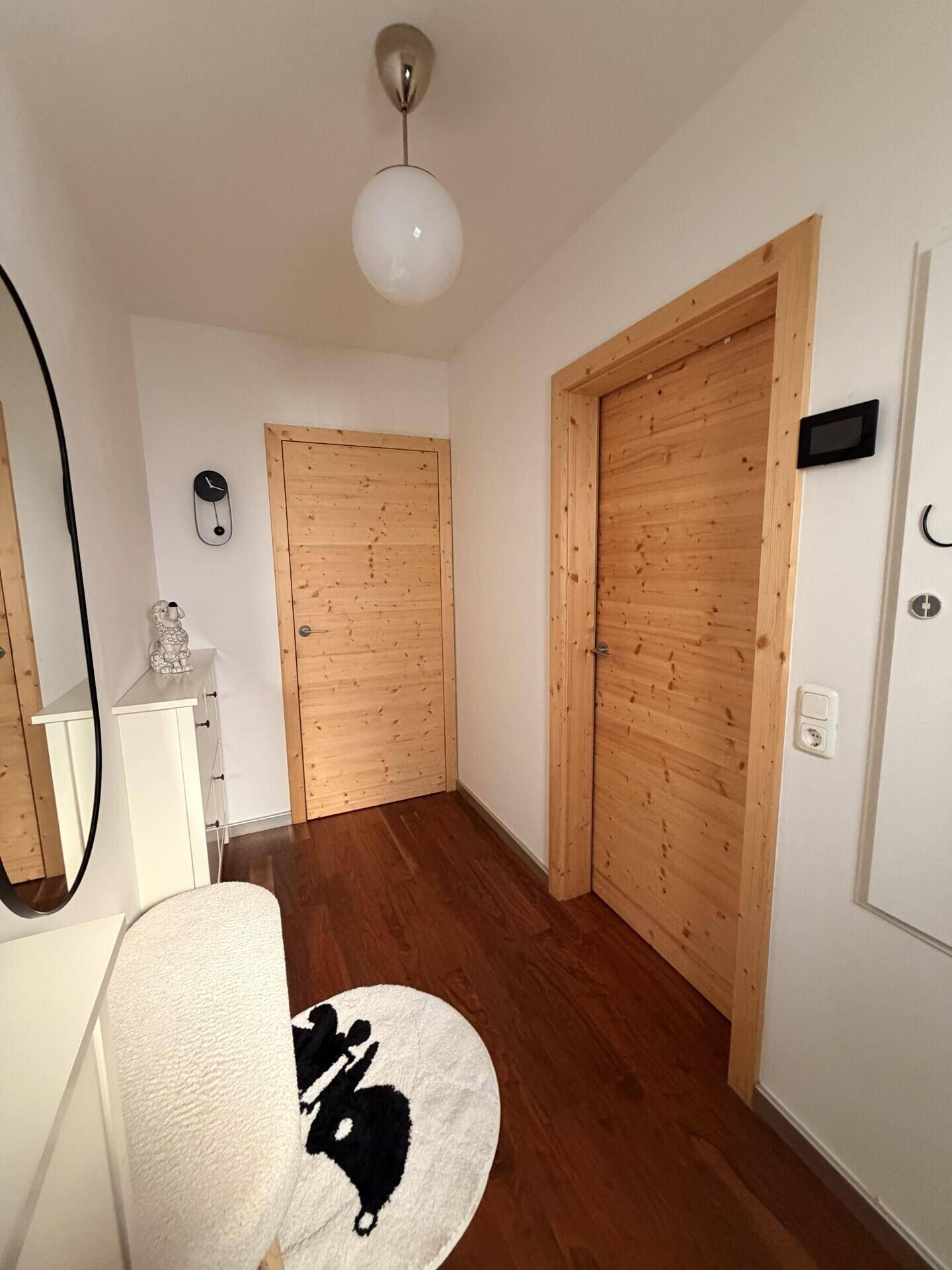 Heller Flur mit Holztüren und dunklem Holzboden, minimalistisch eingerichtet.