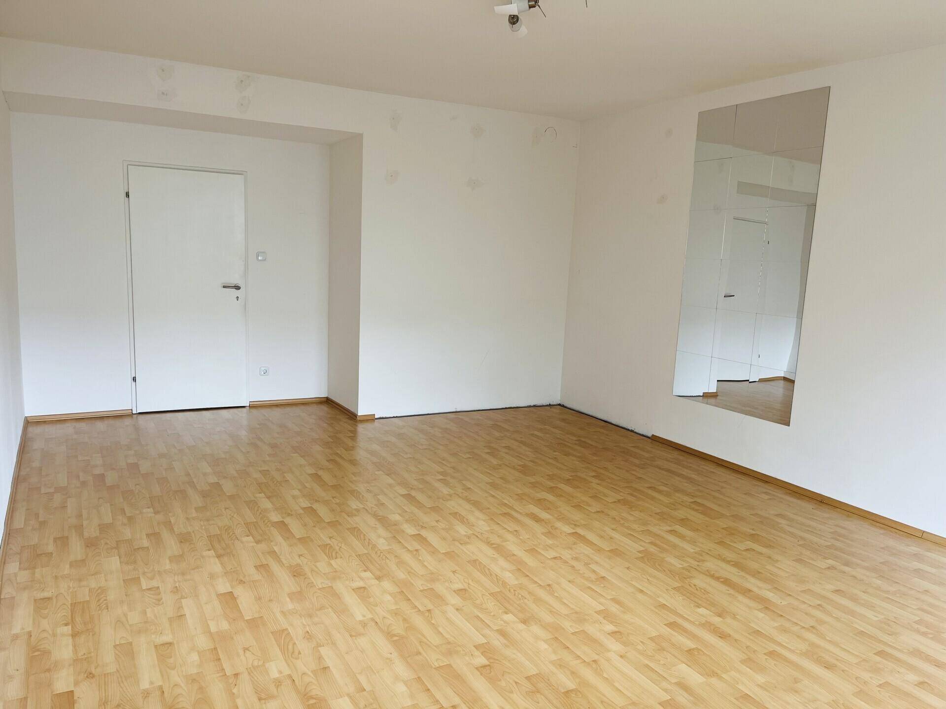 Wohnzimmer mit Parkettboden, weiß gestrichenen Wänden und Spiegelfläche.