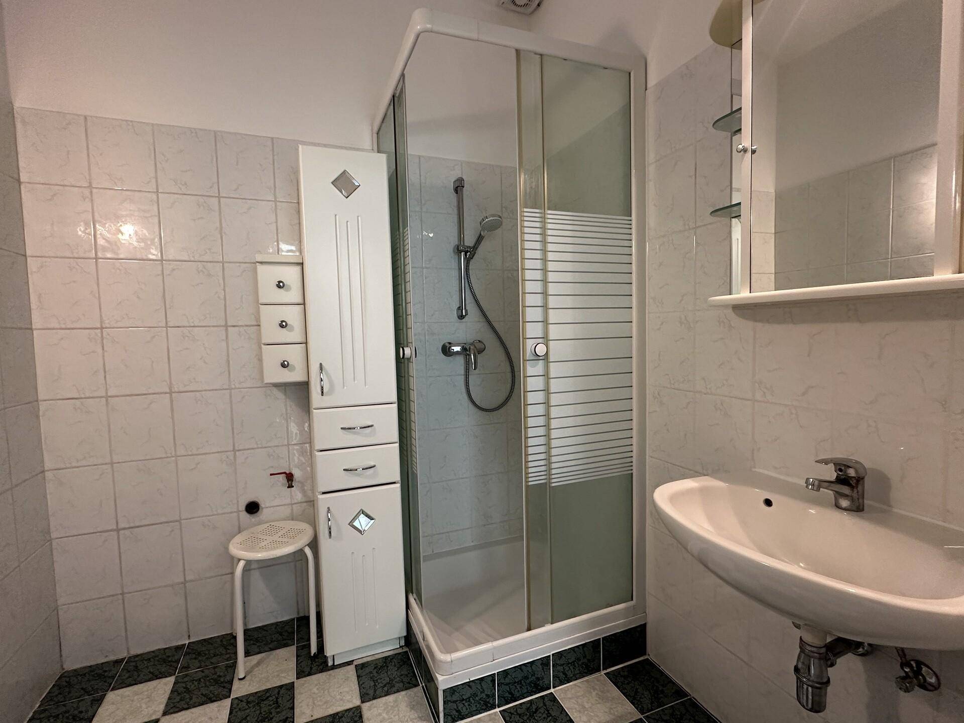 Badezimmer mit Duschkabine, Waschbecken und weiß-grün kariertem Fliesenboden.