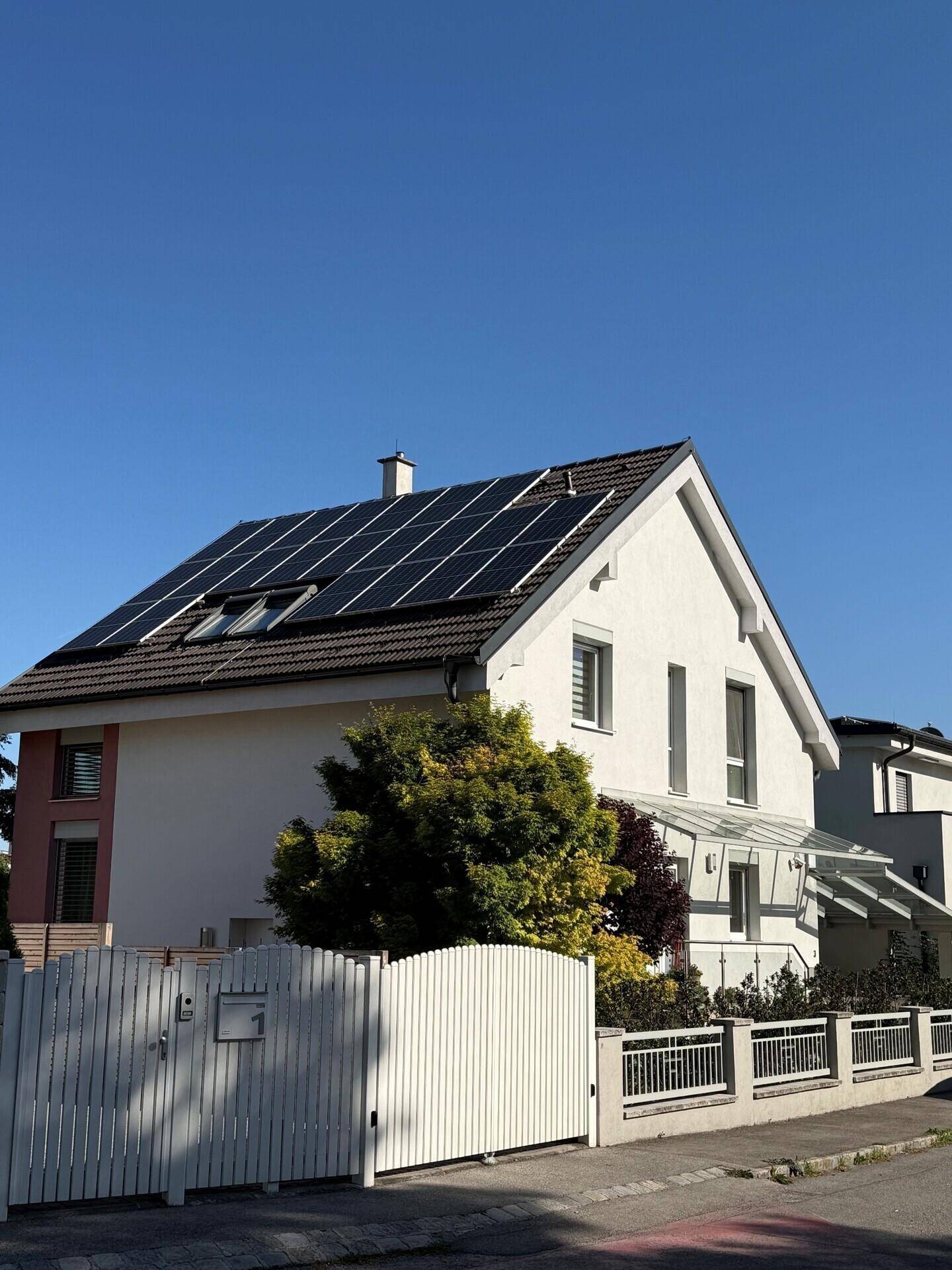 Vorderansicht des Hauses mit Photovoltaikanlage auf dem Dach und weißem Gartenzaun.