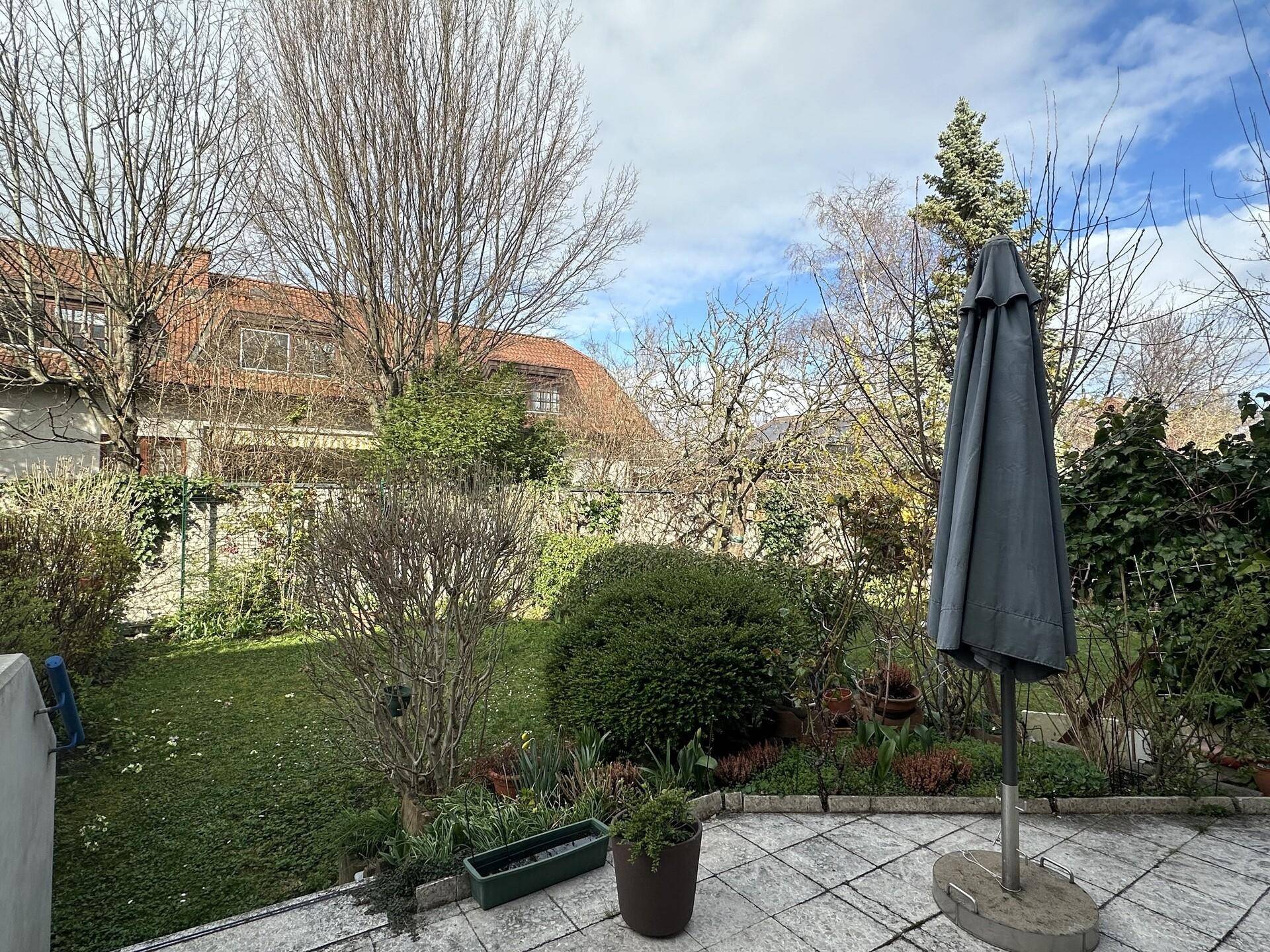 Terrasse mit Fliesenboden, Sonnenschirm und Blick auf den grünen Gartenbereich.