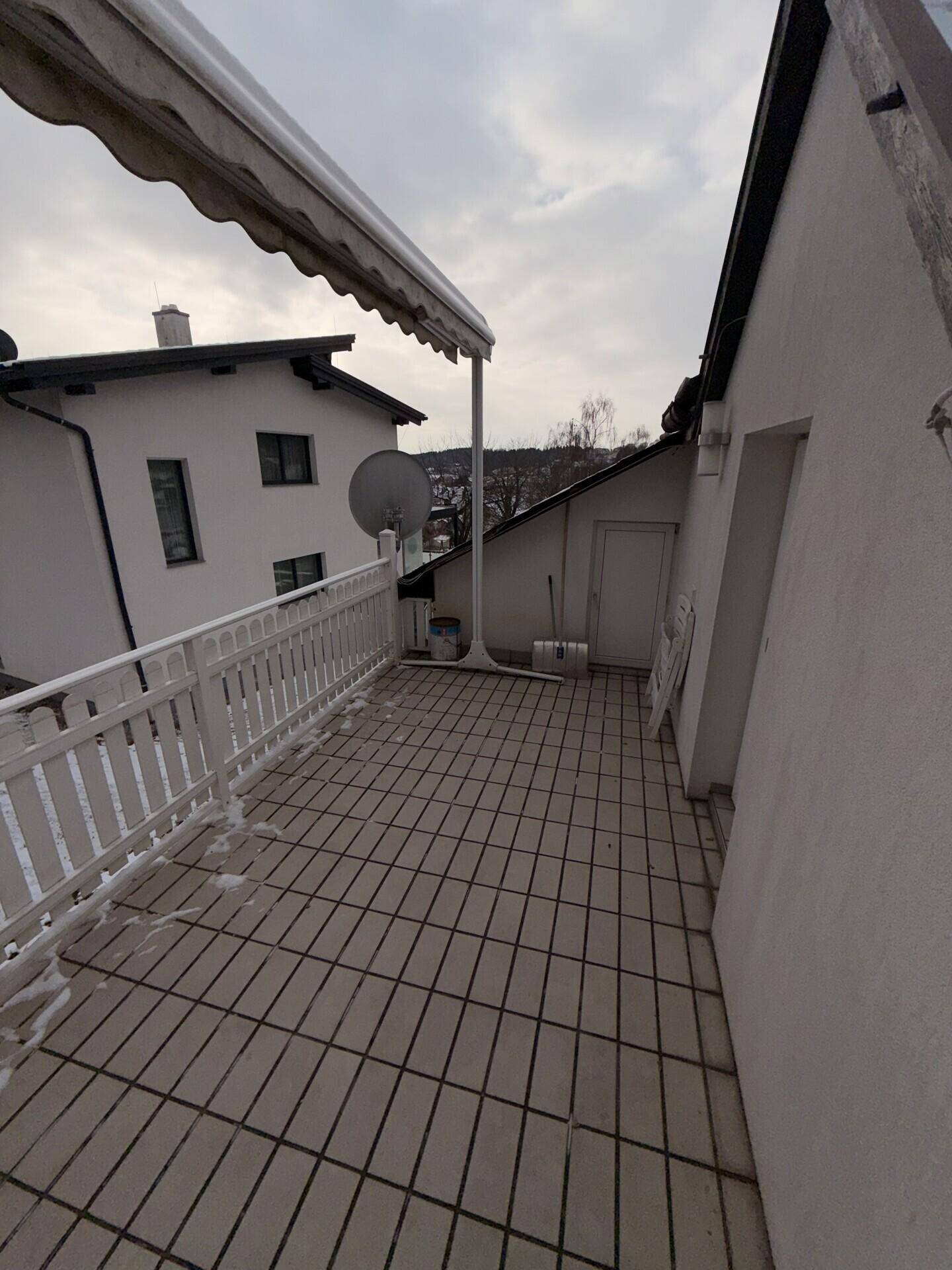 Leerer Balkon im Winter mit Fliesenboden und Blick auf die verschneite Umgebung.