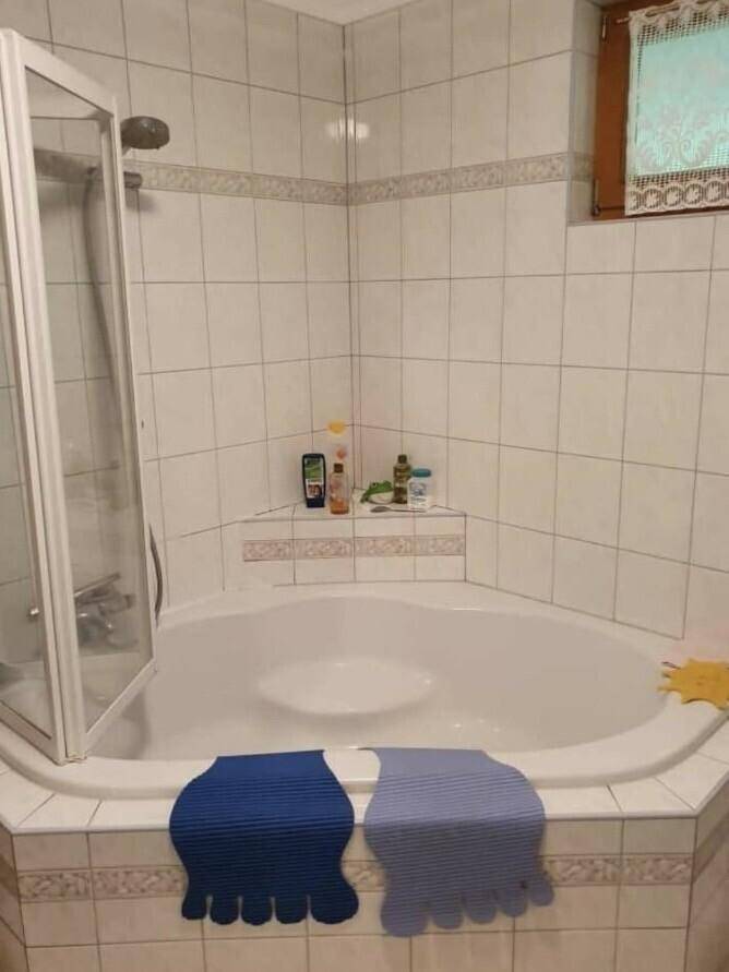 Badezimmer mit Eckbadewanne, Duschabtrennung und weißen Wandfliesen.