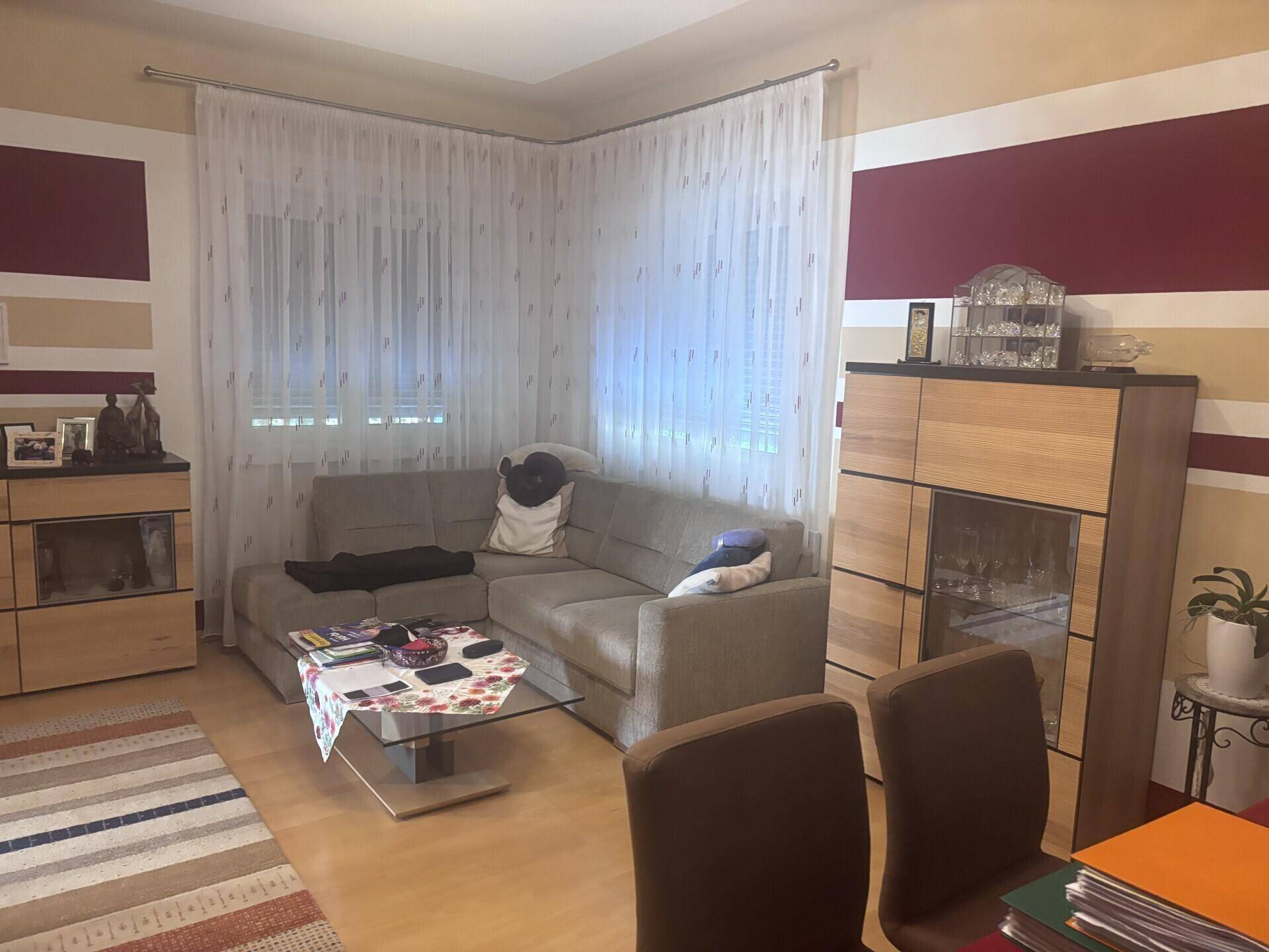 Geräumiges Wohnzimmer mit beigem Ecksofa, Holzboden und dekorativen Wandstreifen in Rot und Beige.