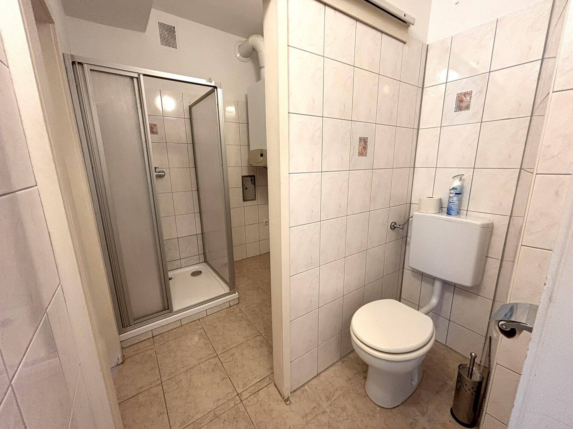 Badezimmer mit Duschkabine und Toilette, ausgestattet mit hellen Fliesen und funktionaler Einrichtung.