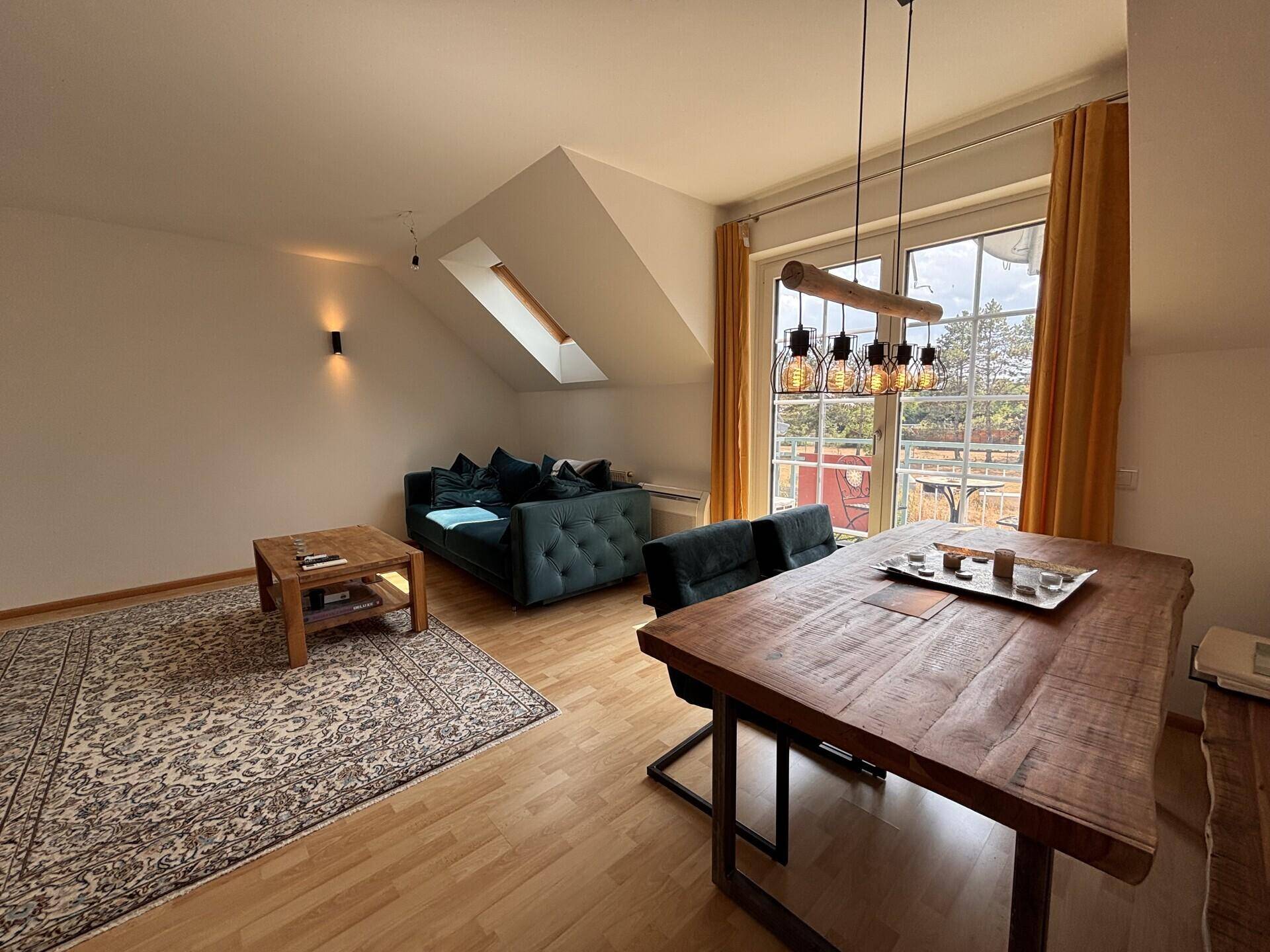 Heller Wohn-Essbereich mit Holztisch, dunkelgrünem Sofa und Zugang zu einem Balkon.