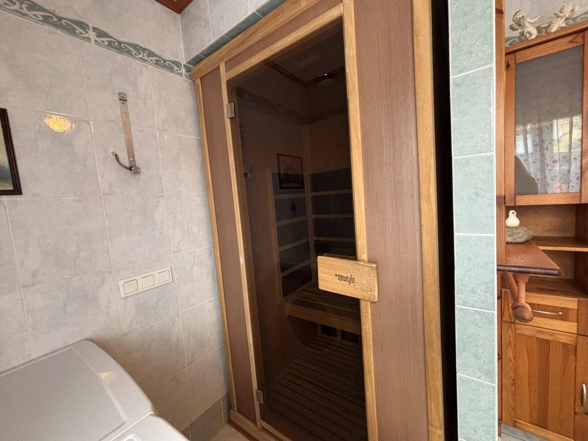 Badezimmer mit integrierter Holzsauna, Fliesenwänden und einem Spiegelschrank.
