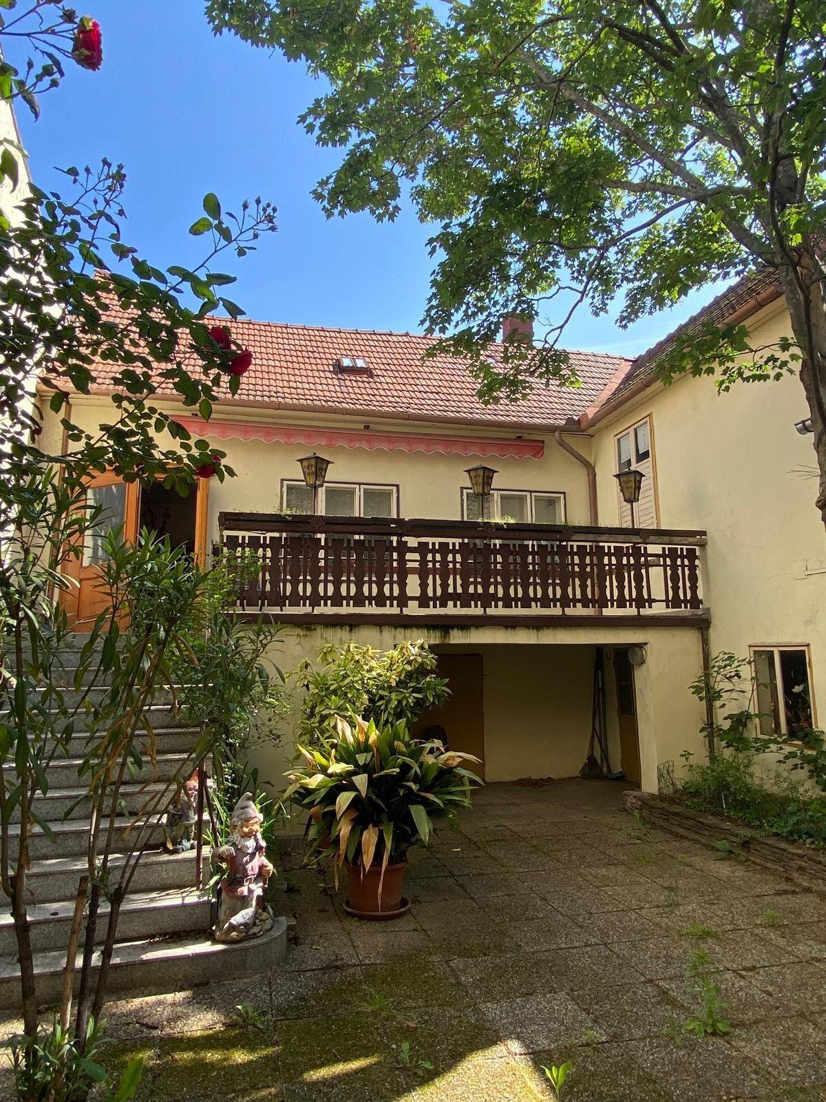 Sonniger Hinterhof mit üppigem Grün, gepflastertem Bereich und einem Balkon am Gebäude.