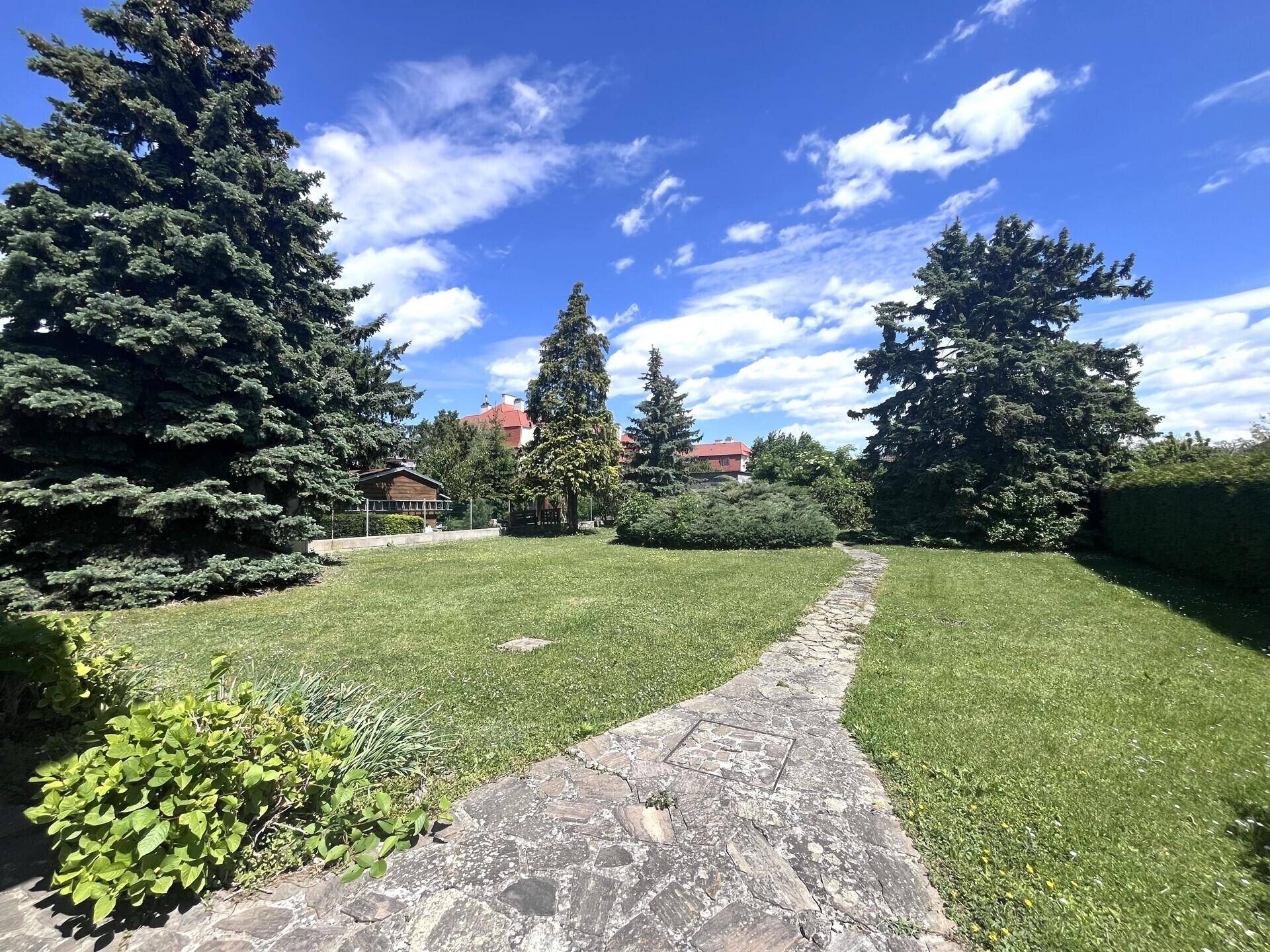 Großer, gepflegter Garten mit Rasenfläche, hohen Bäumen und einem malerischen Steinweg.