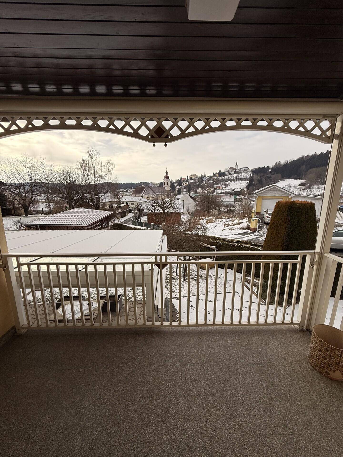 Blick vom überdachten Balkon auf die winterliche Landschaft und das verschneite Dorf.