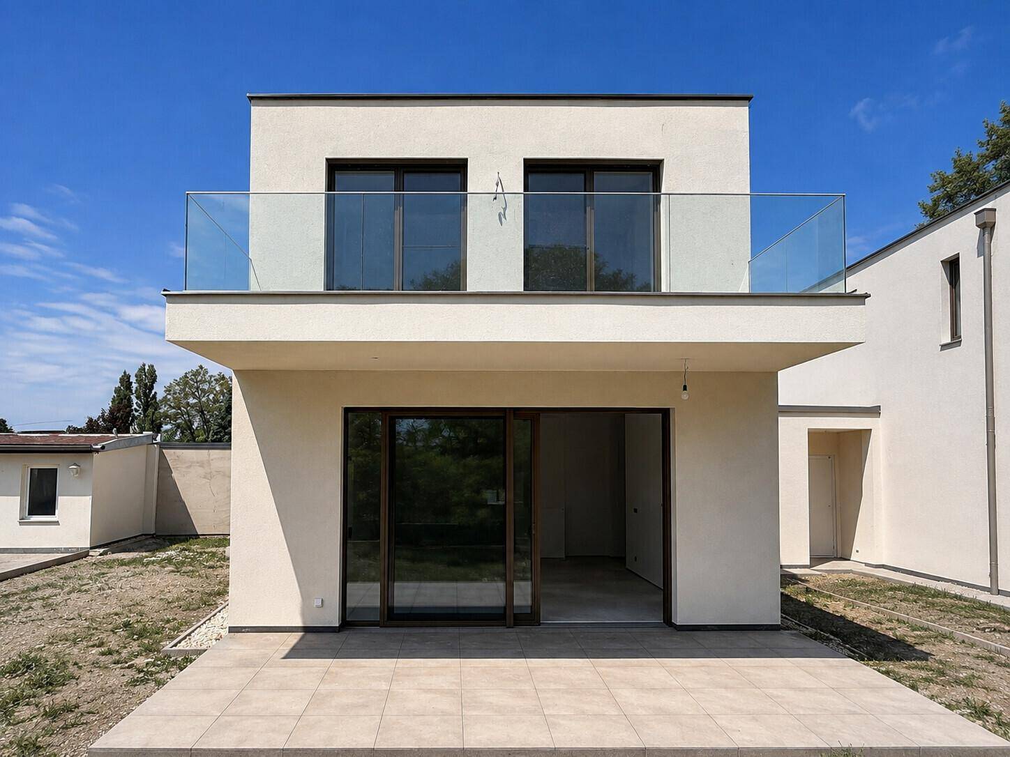 Rückseite des modernen Hauses mit großer Terrasse im Erdgeschoss und Balkon mit Glasgeländer im Obergeschoss.