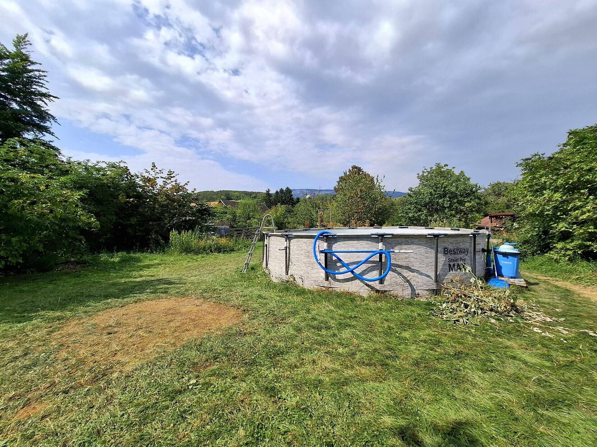 Aufgestellter Pool im weitläufigen Garten, umgeben von üppigem Grün und Bäumen.