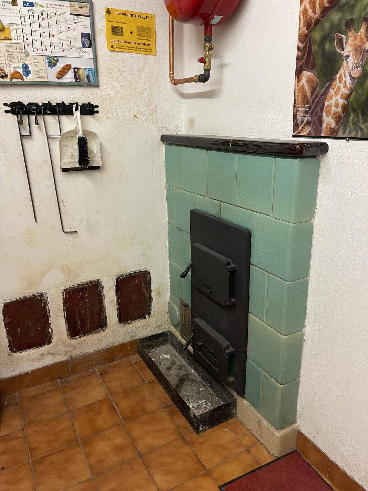Grüner Kachelofen in einem Nebenraum, möglicherweise im Keller oder Heizraum.