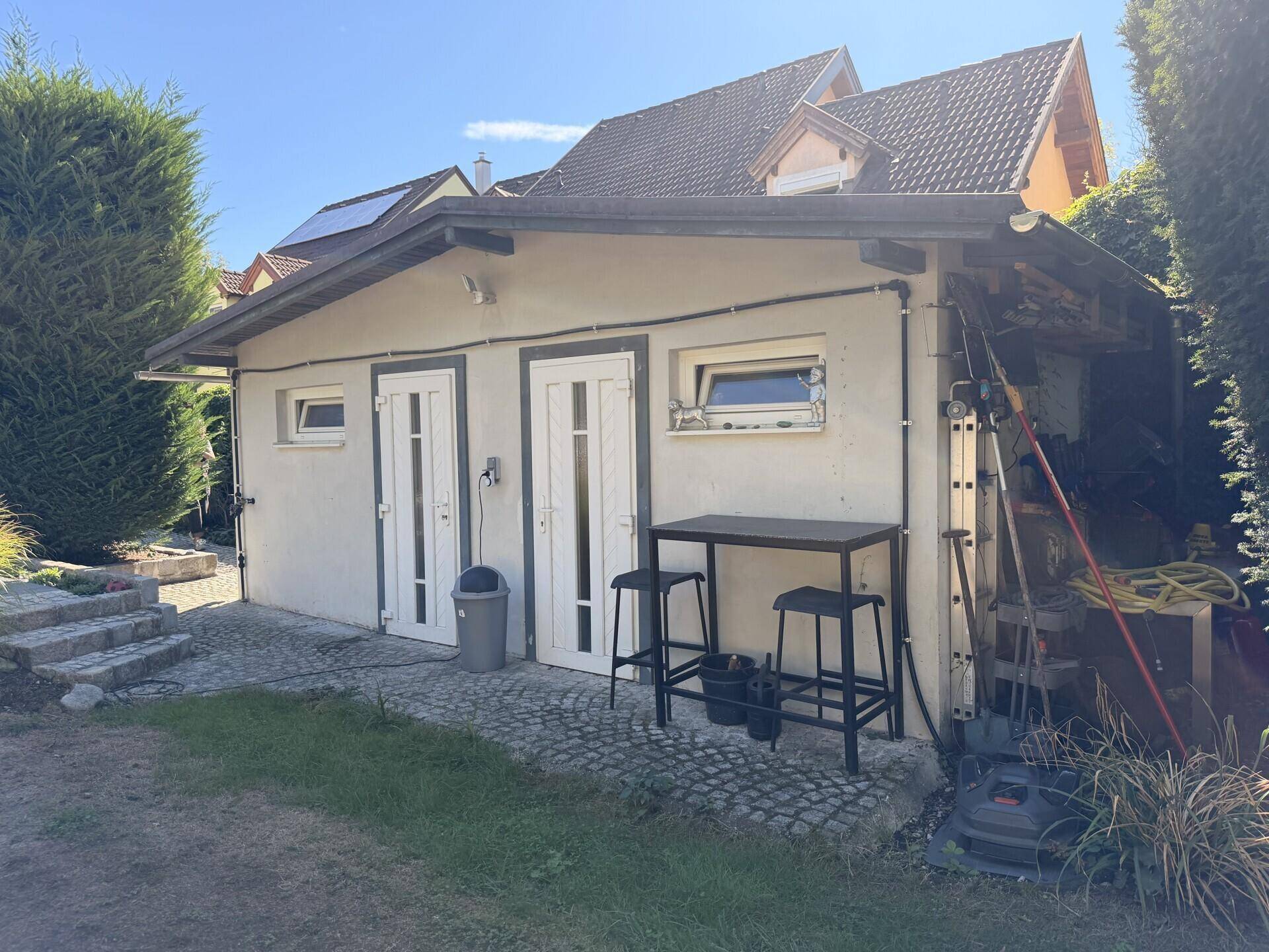 Kleines Nebengebäude im Garten mit zwei Türen und Außenbereich für Werkzeuge.