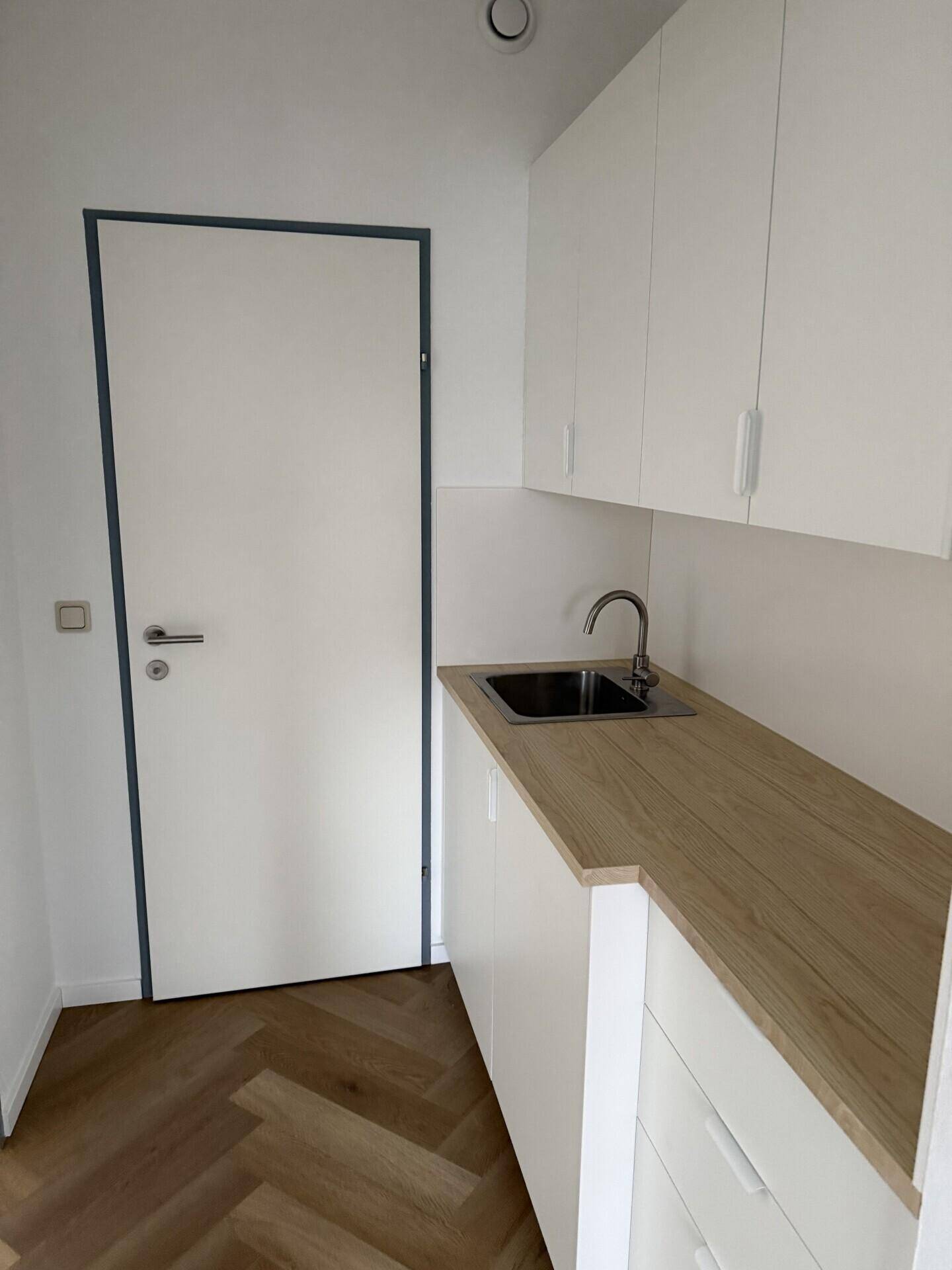 Kleine Küchenzeile mit weißen Schränken, einer Arbeitsplatte aus Holz und einer Spüle.