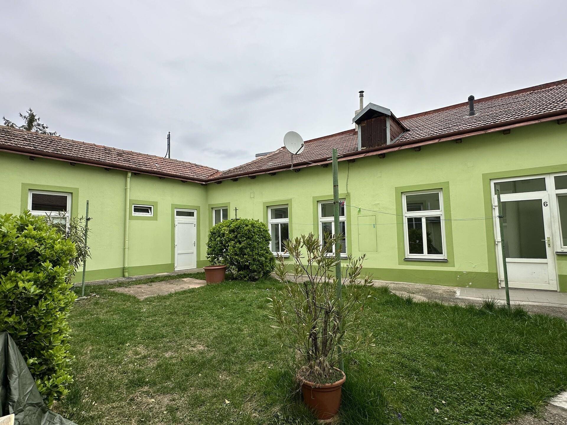 Hinterhof mit Rasenfläche und verschiedenen Fenstern und Türen, die zum Garten führen.