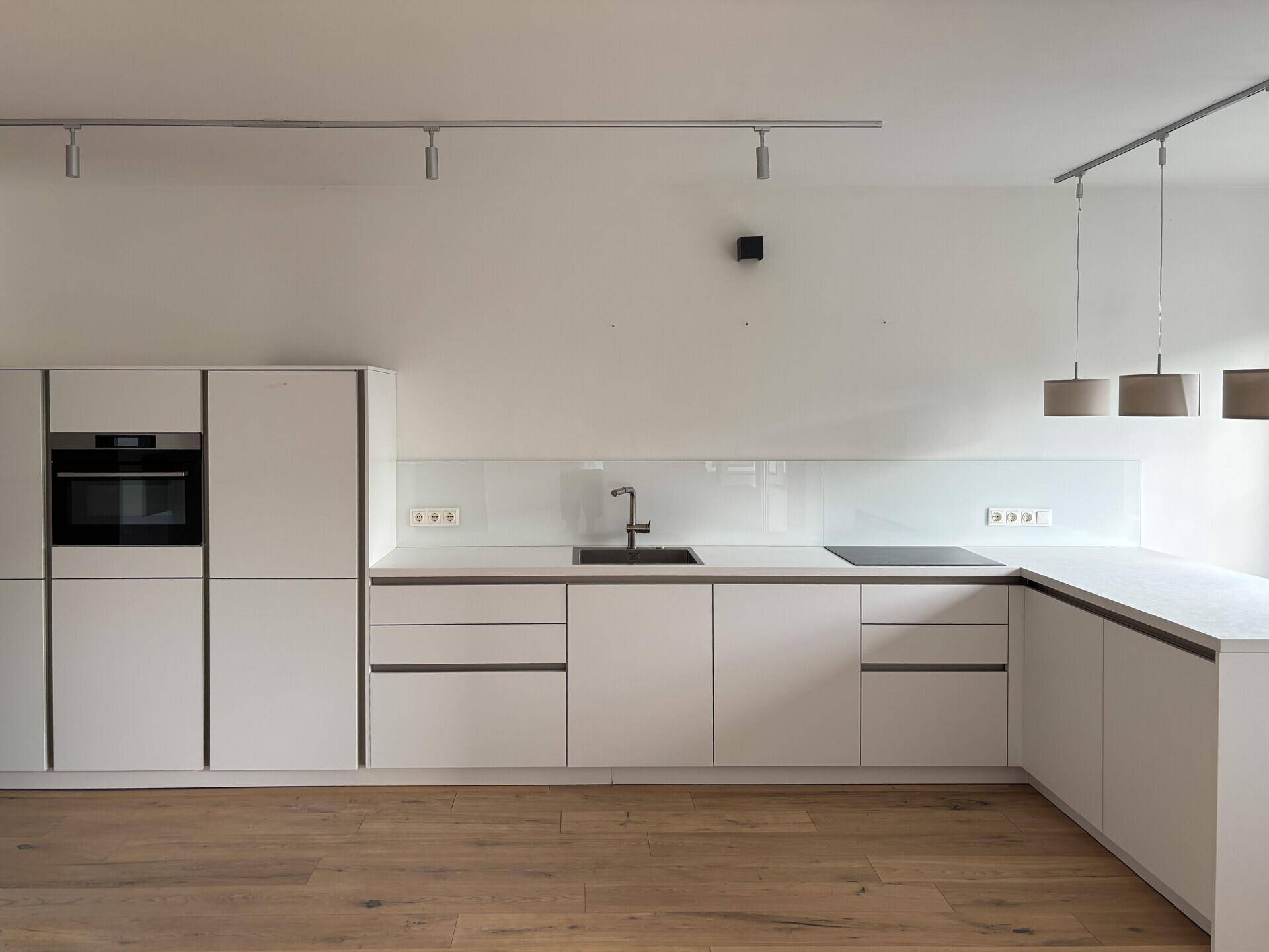 Moderne Einbauküche in Weiß mit integriertem Backofen und Induktionskochfeld.