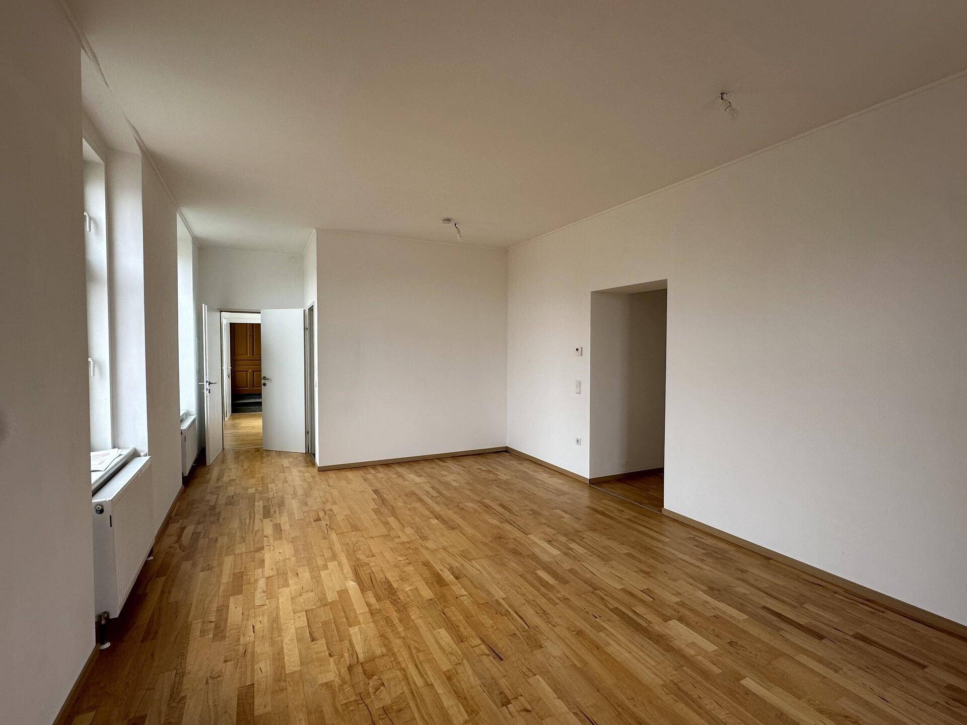 Geräumiges Wohnzimmer mit Parkettboden und Zugang zu weiteren Räumen, bietet viel Platz.