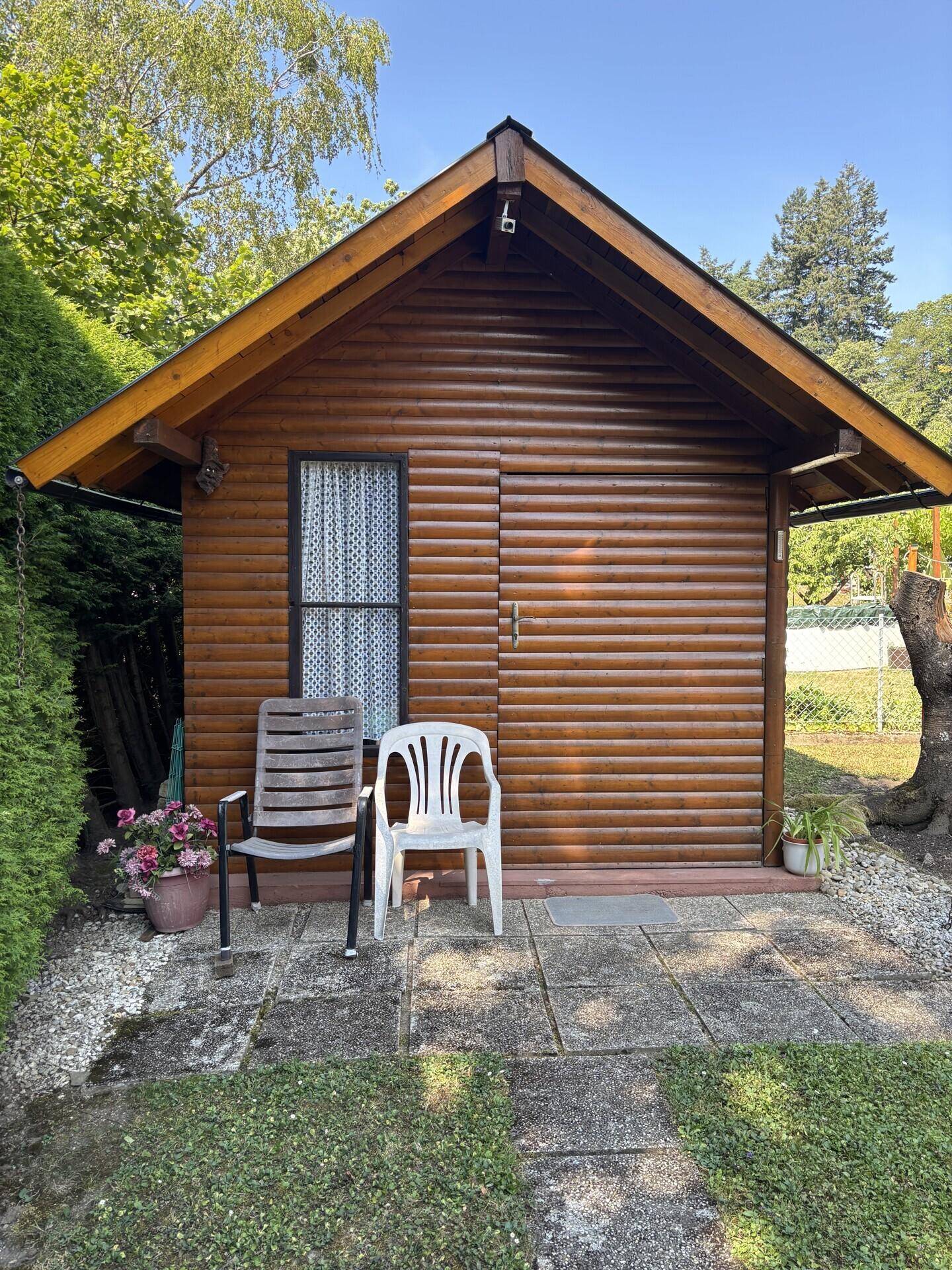 Rustikales Gartenhaus aus Holz mit kleiner Terrasse und Sitzgelegenheiten.