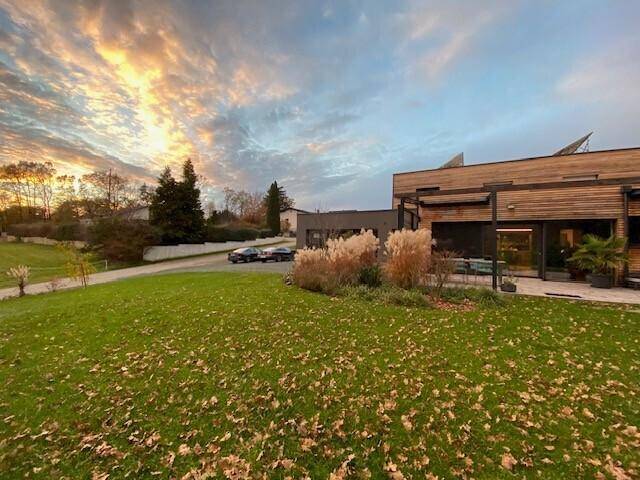 Modernes Haus mit Holzfassade und herbstlichem Garten bei Sonnenuntergang.