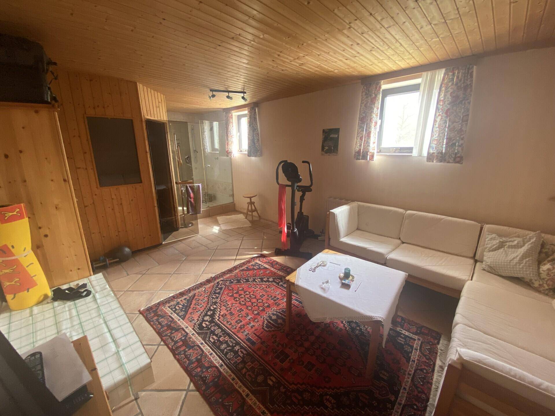Gemütlicher Wohnbereich im Untergeschoss mit Holzdecke, Fliesenboden und Sofa.