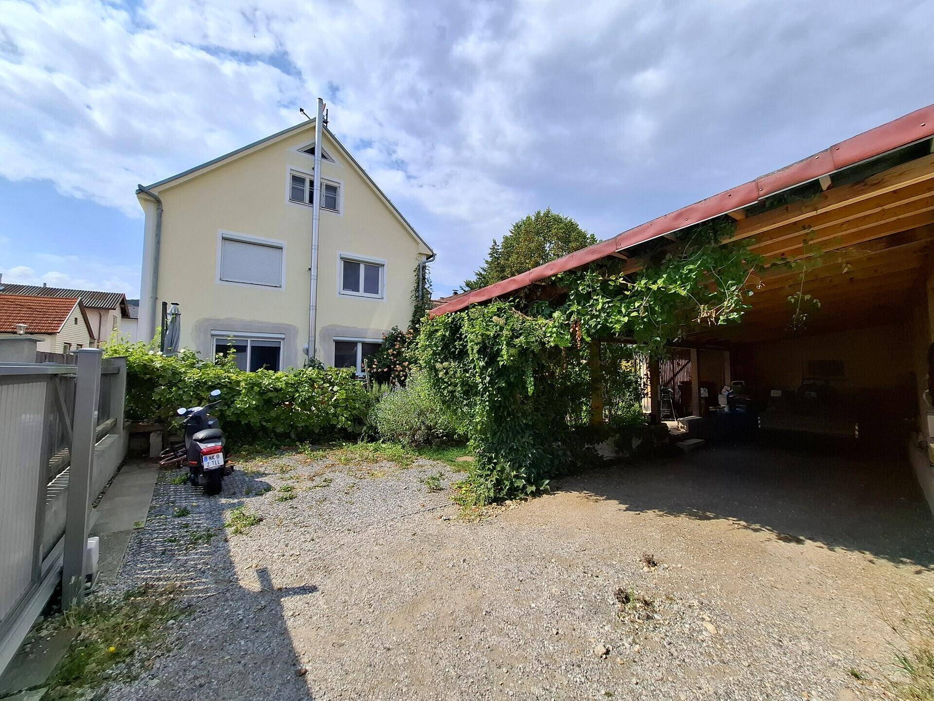Geräumiger Carport und Einfahrt zum Haus, umgeben von grüner Bepflanzung.