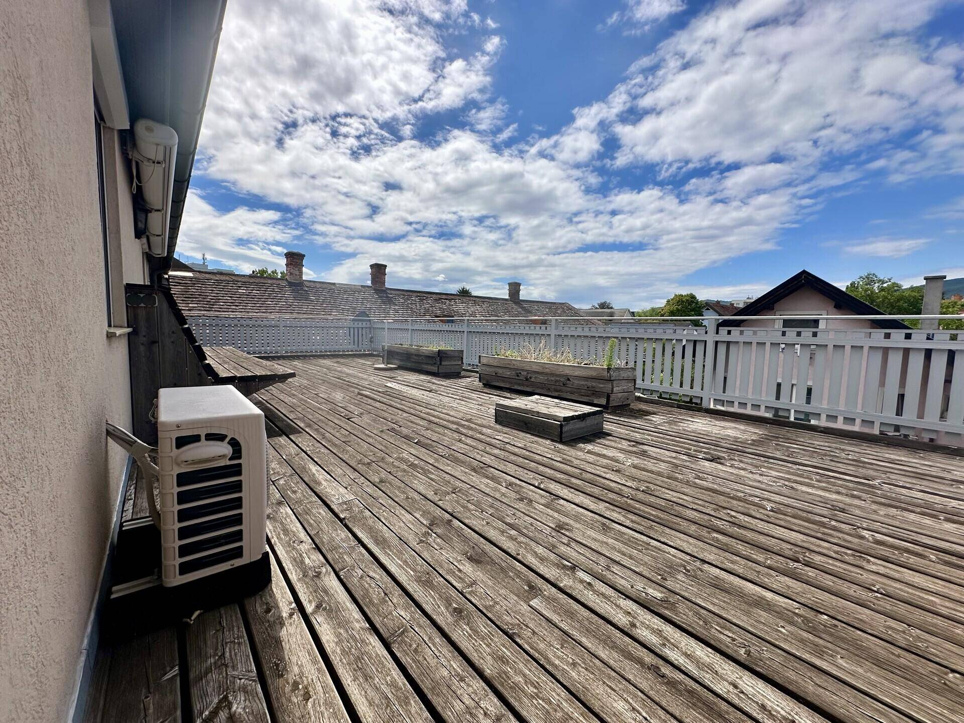 Dachterrasse mit Holzboden, weißem Geländer und einer Klimaanlage im Freien.