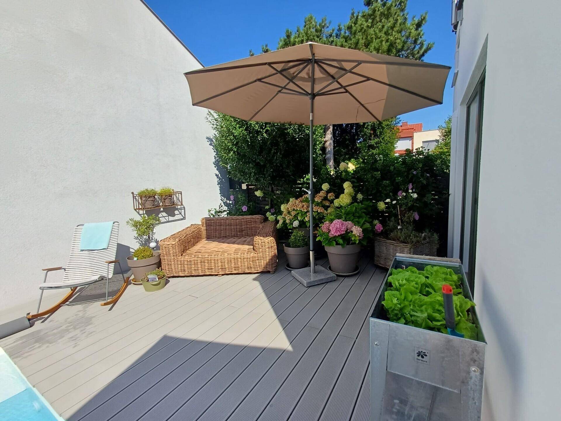 Sonniger Terrassenbereich mit Holzdeck, Sonnenschirm und einem Hochbeet für frisches Gemüse.