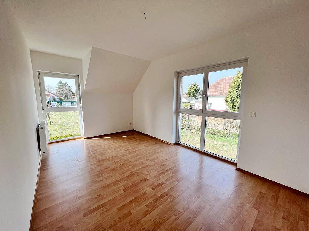 Weiteres helles Schlafzimmer mit Laminatboden, zwei Fenstern und Dachschräge, bietet viel Tageslicht.