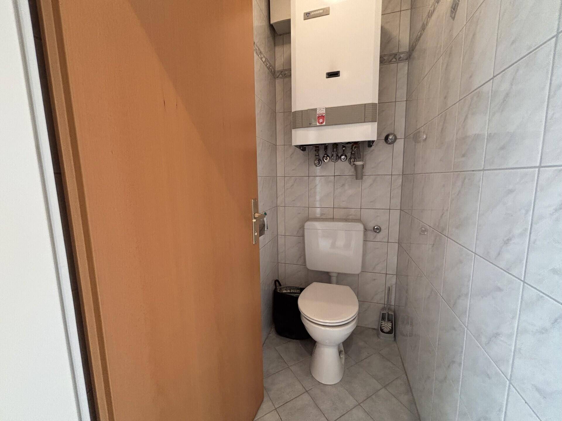 Kleines WC mit weißen Fliesen, Toilette und wandmontiertem Warmwasserbereiter.