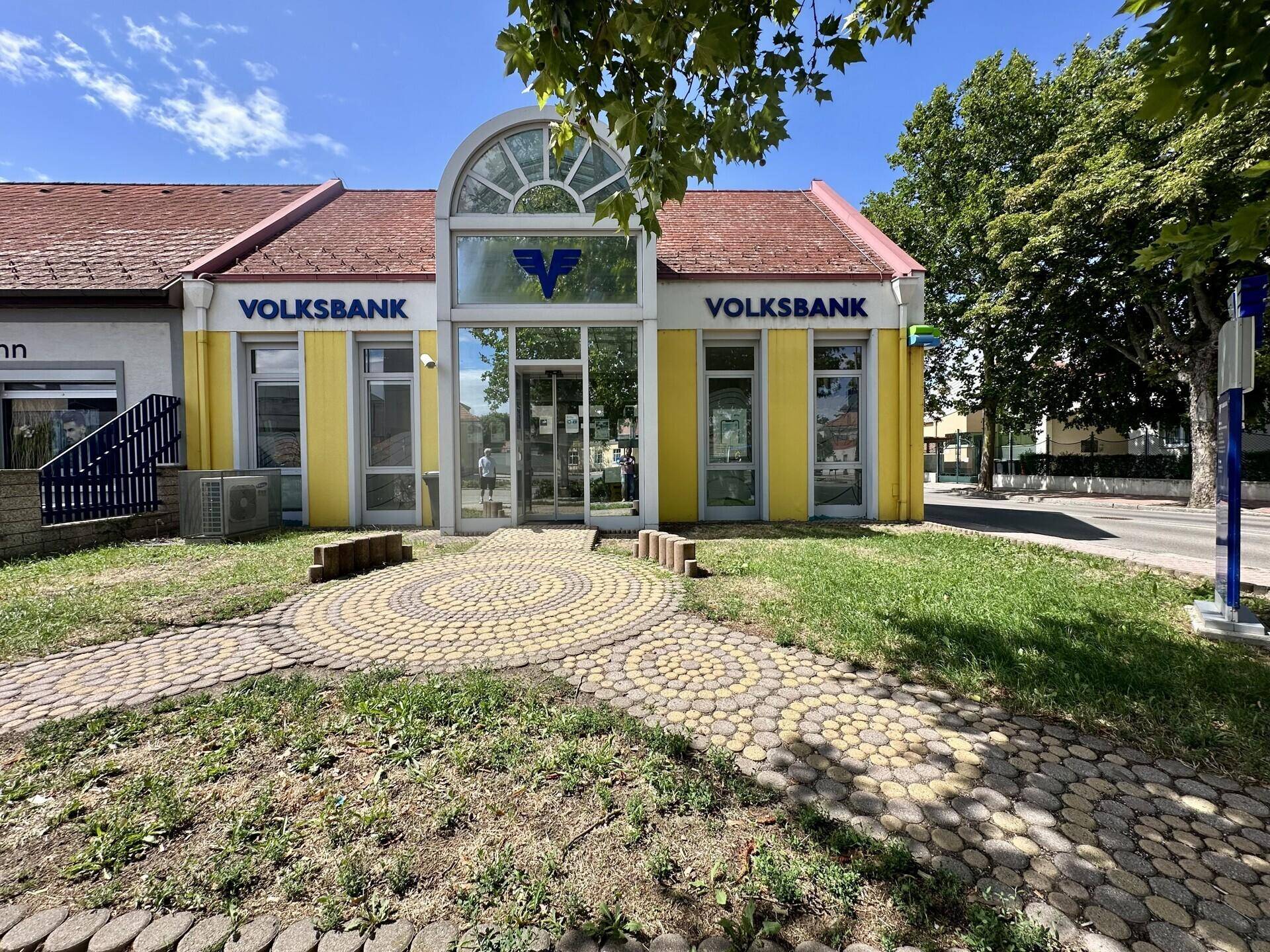 Vorderansicht des Bankgebäudes mit gepflastertem Eingangsbereich und grüner Rasenfläche.