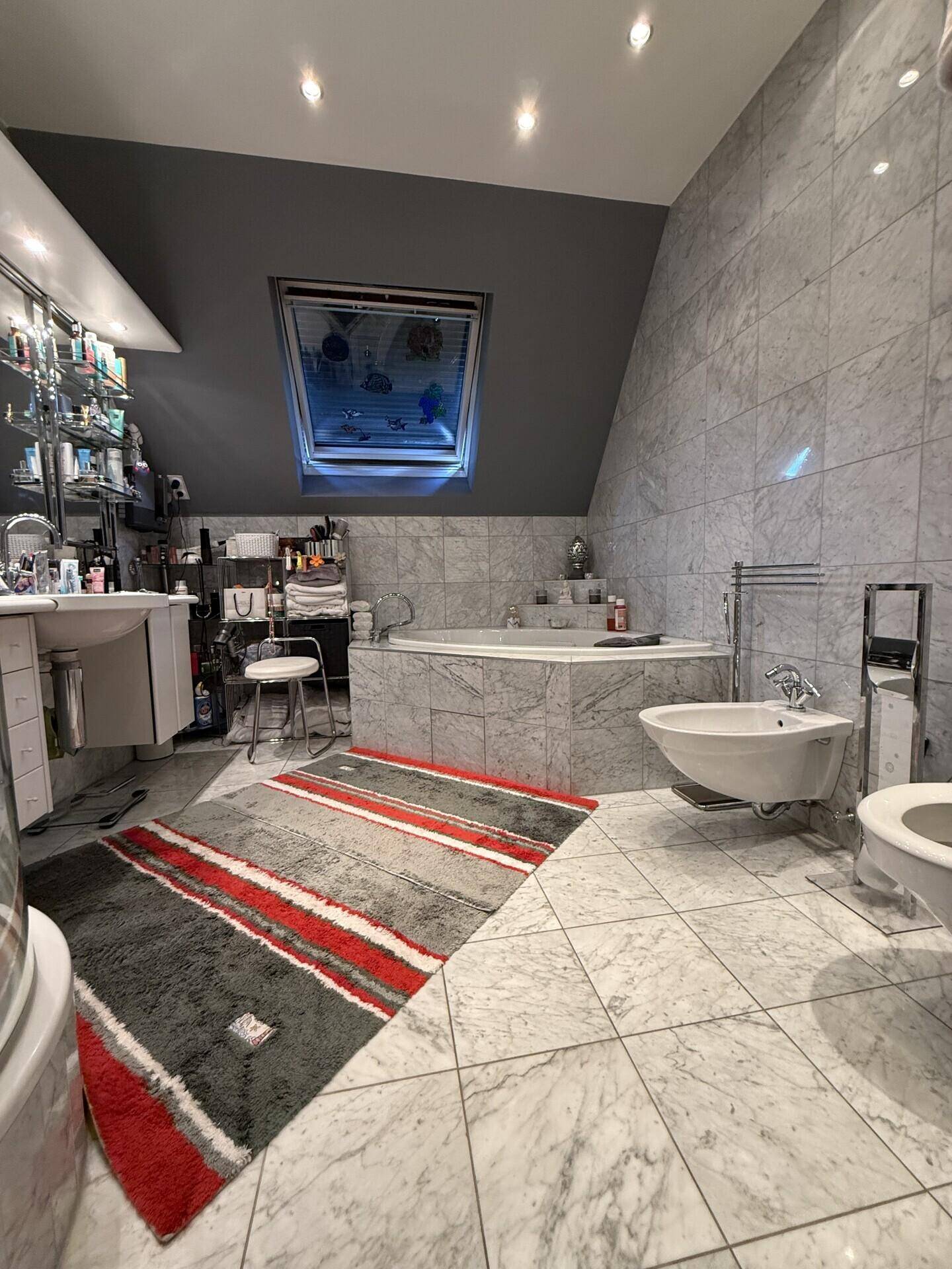 Großes Badezimmer mit Marmorfliesen, Eckbadewanne, Bidet und Dachfenster.