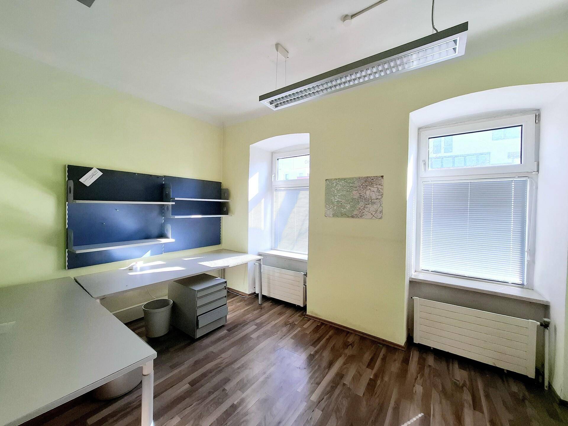 Büro mit gelben Wänden, Holzboden und zwei Fenstern, ausgestattet mit Schreibtischen und Regalen.
