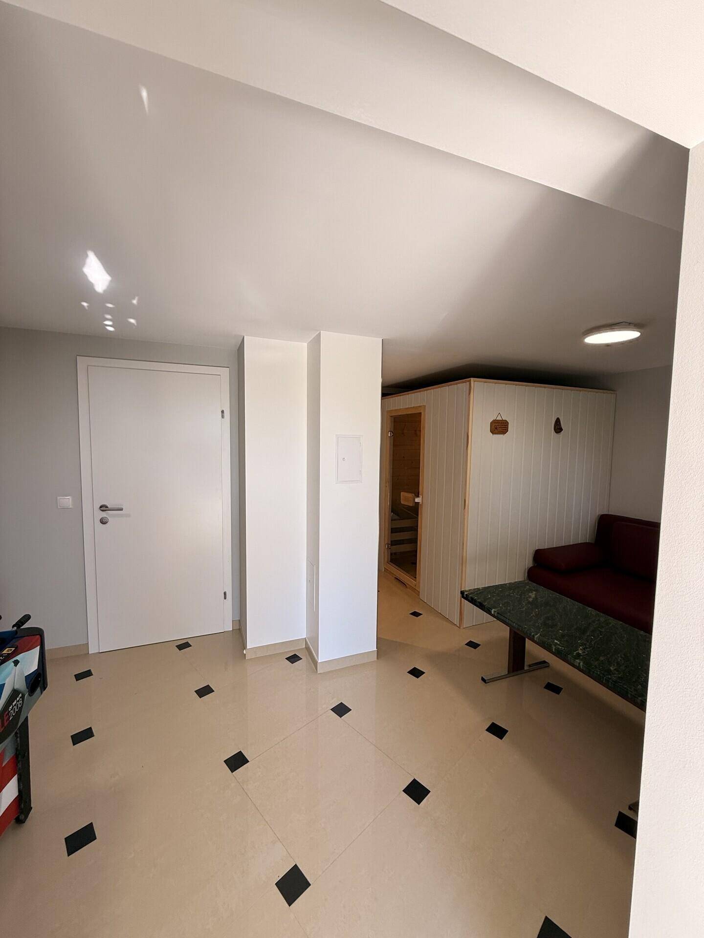 Entspannungsbereich mit Sauna, rotem Sofa und Fliesenboden.