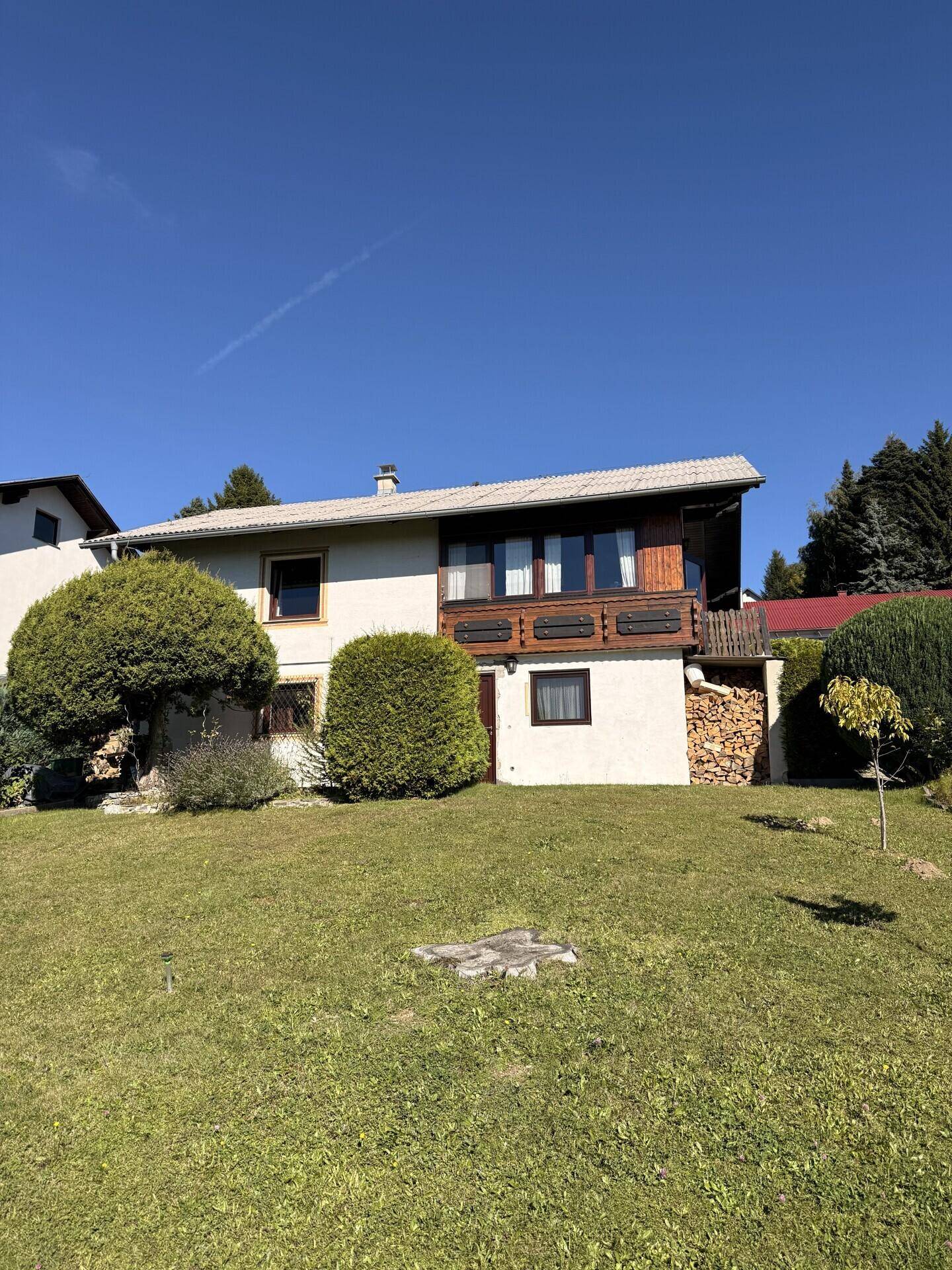 Ansicht des Hauses von der Gartenseite mit Balkon und gestapeltem Brennholz.