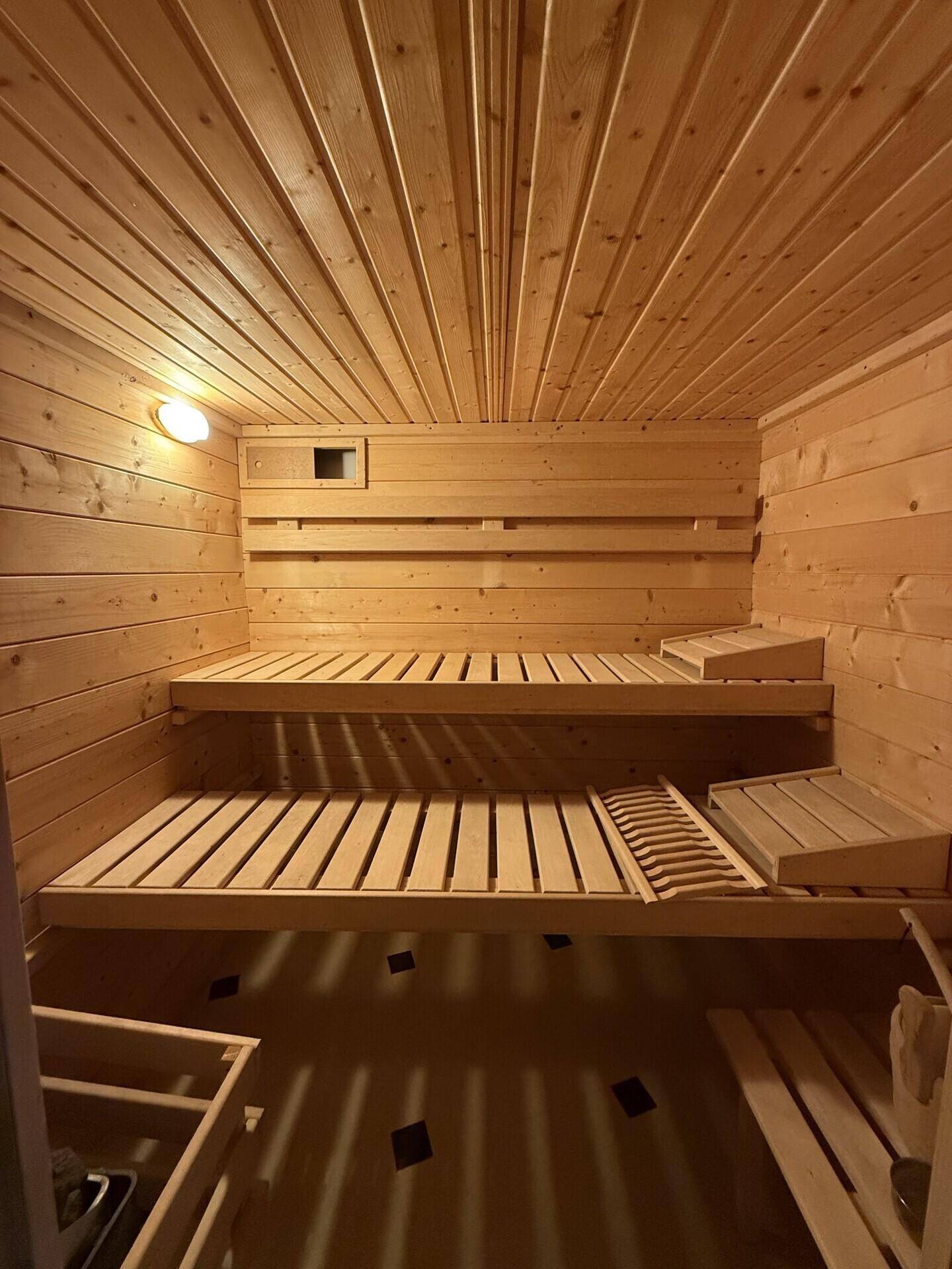 Innenansicht der Holzsauna mit zwei Ebenen von Sitzbänken und warmer Beleuchtung.
