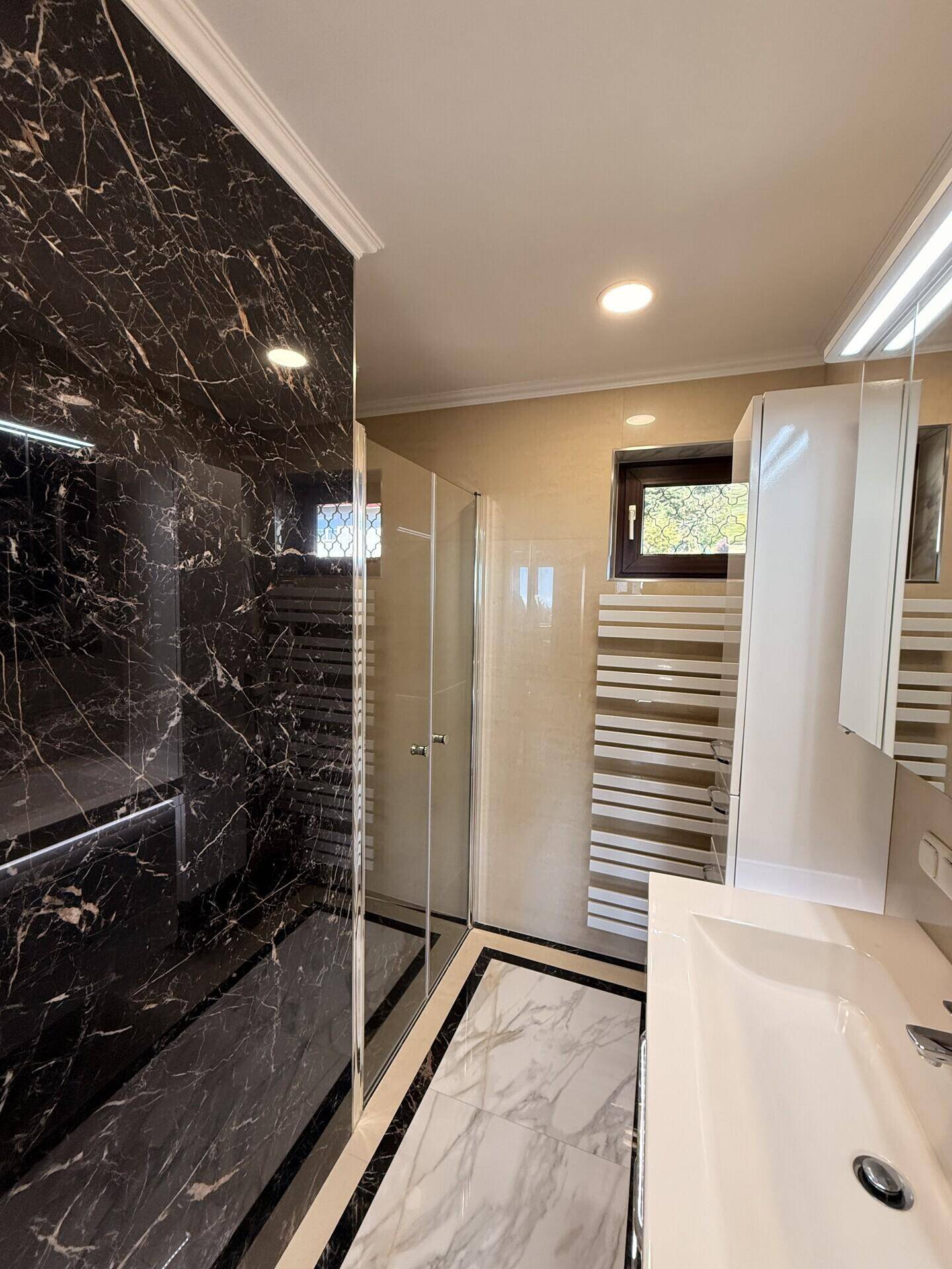 Elegantes Badezimmer mit dunklen Marmorfliesen in der Dusche und hellem Waschtischbereich.