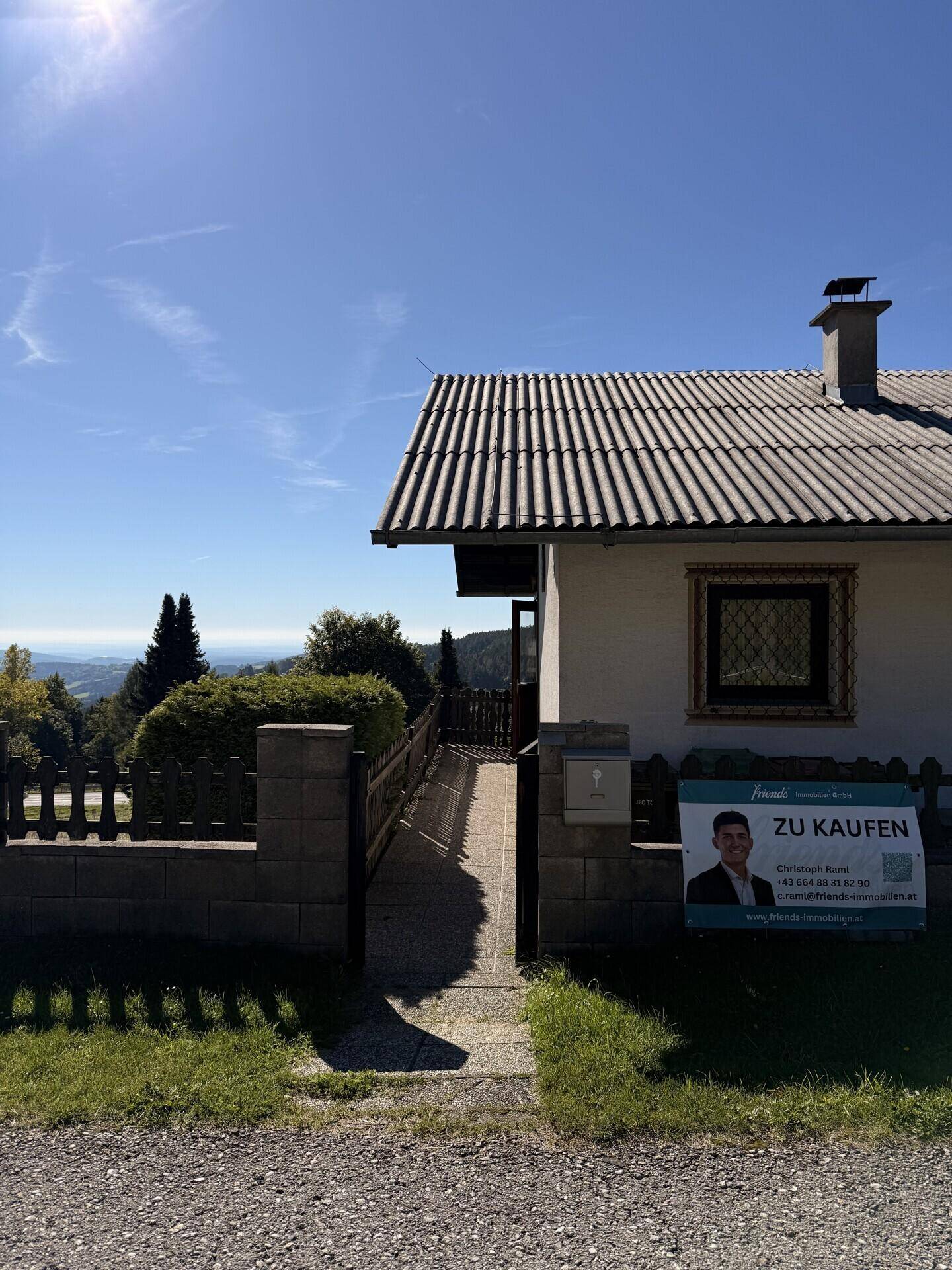 Eingangsbereich des Hauses mit gepflastertem Weg, Zaun und "Zu Kaufen"-Werbeschild.