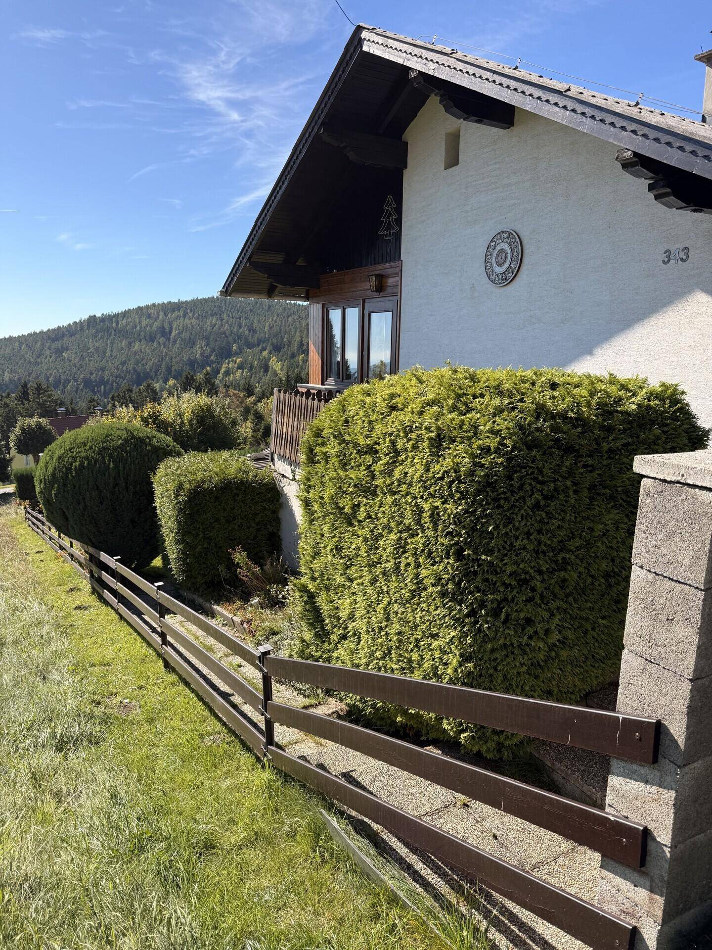Traditionelles Haus mit weißer Fassade, Holzbalkonen und gepflegten Hecken.