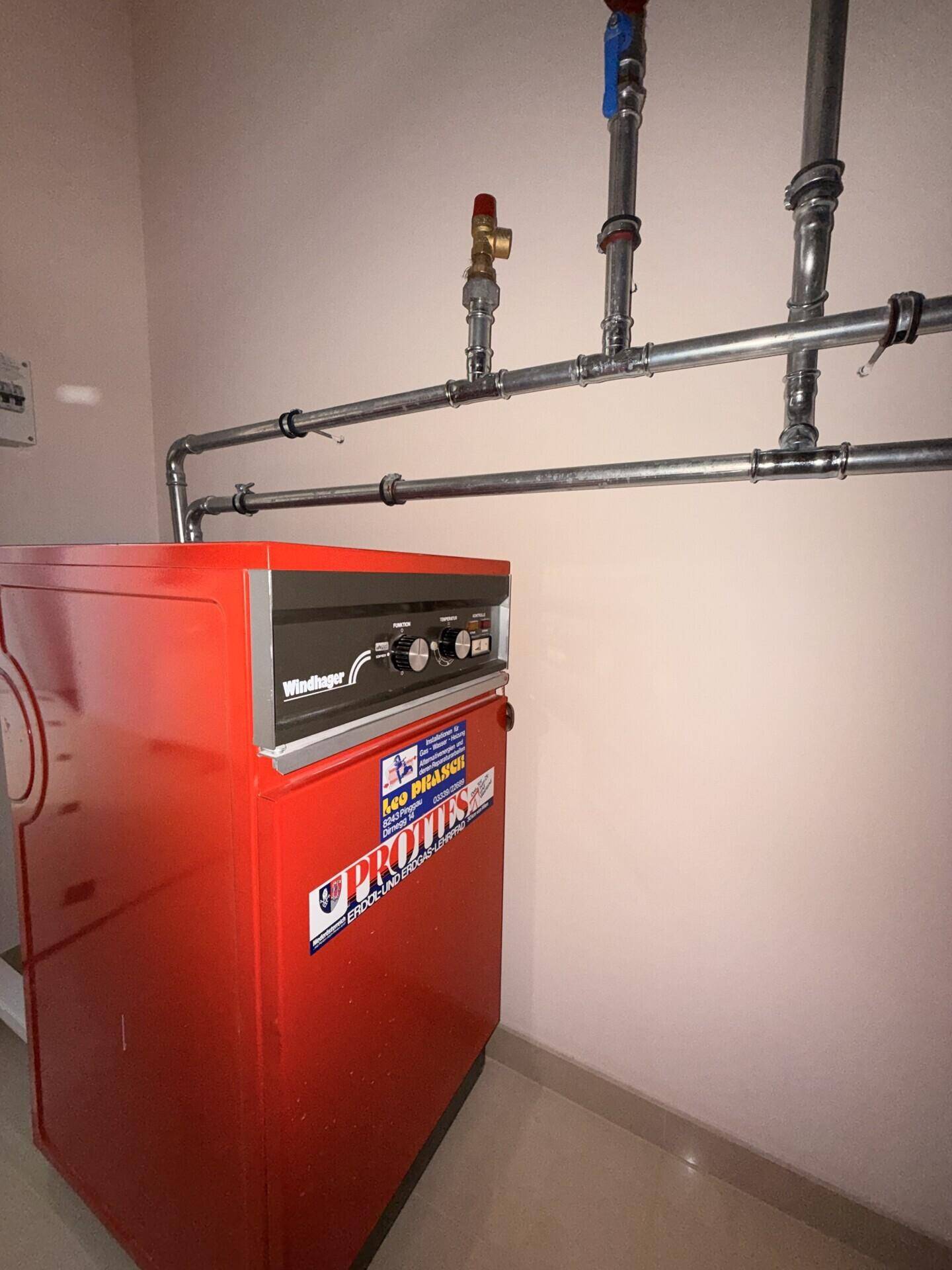 Heizungsraum mit rotem Heizkessel und sichtbaren Rohrleitungen für die Haustechnik.