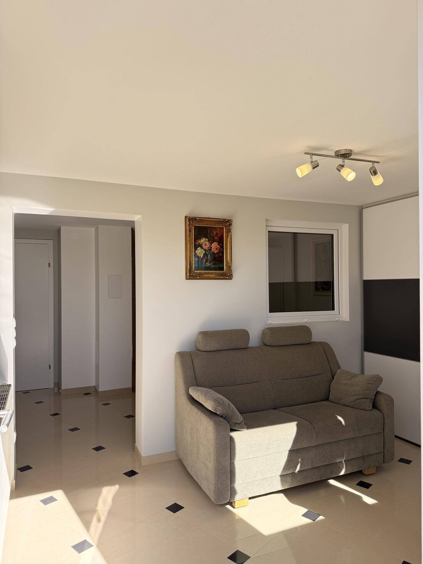 Helles Wohnzimmer mit beigem Sofa, Fliesenboden und Fenster.