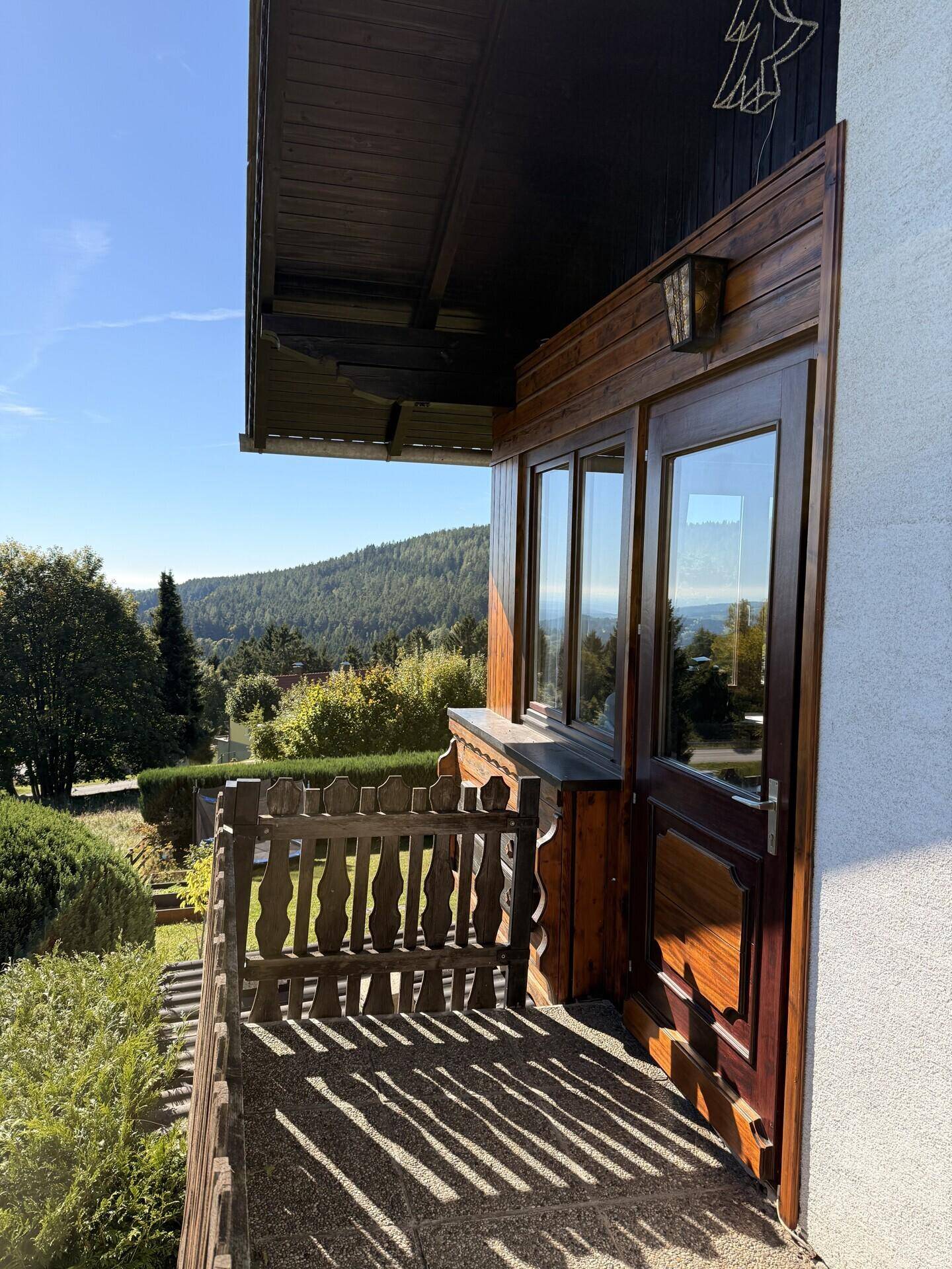 Gemütlicher Balkon mit Holzelementen und weitem Blick auf die bewaldete Hügellandschaft.