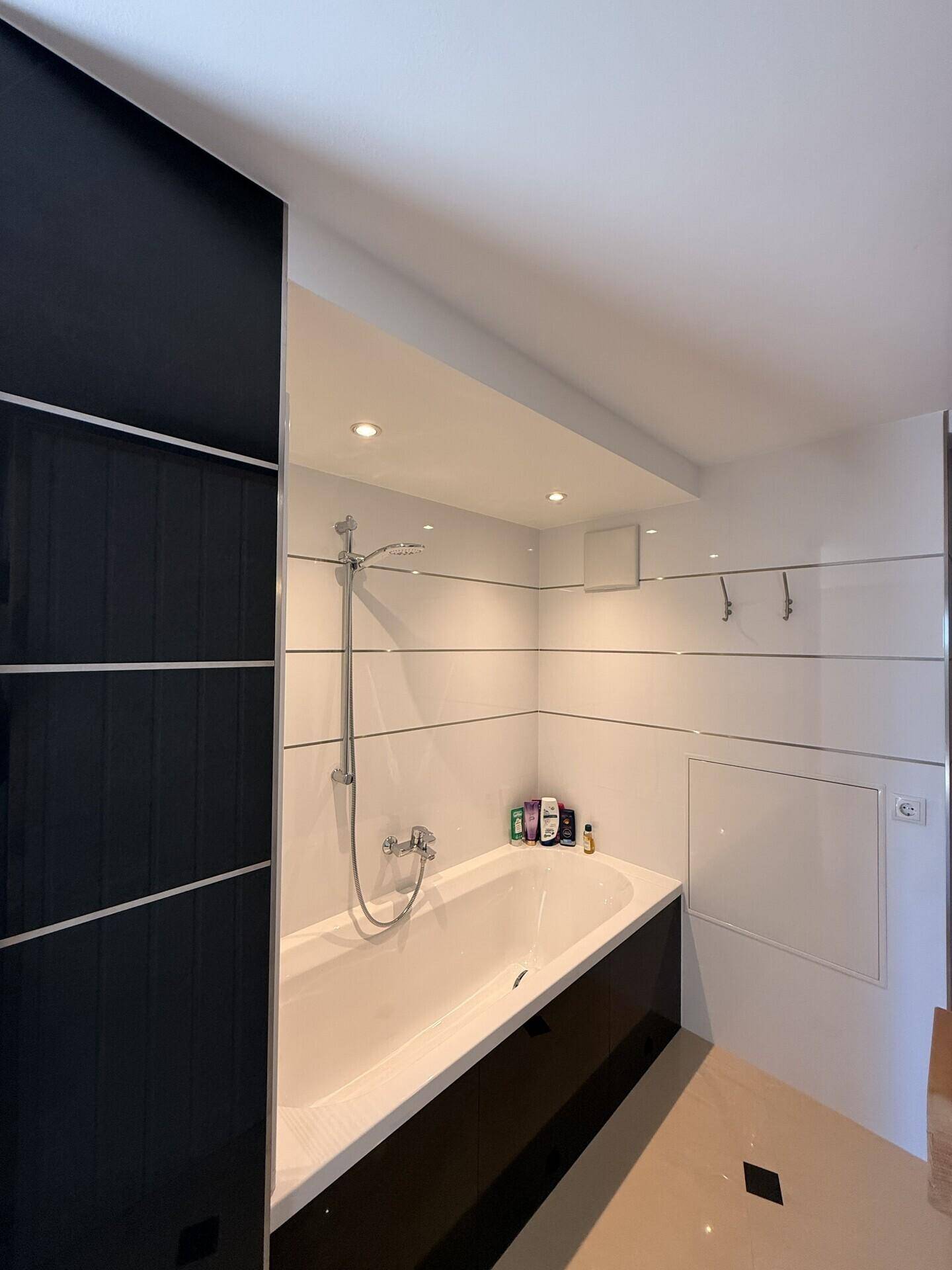 Modernes Badezimmer mit integrierter Badewanne und Duscharmatur, in Schwarz-Weiß-Design.