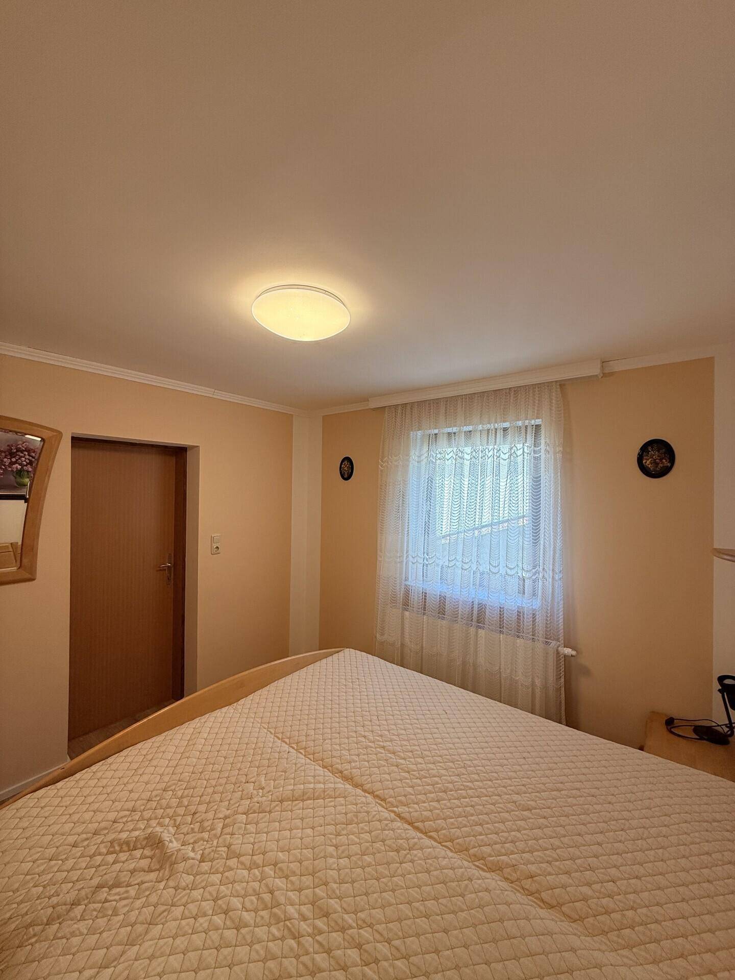 Schlafzimmer mit Doppelbett, hellem Laminatboden und schlichten Wänden.