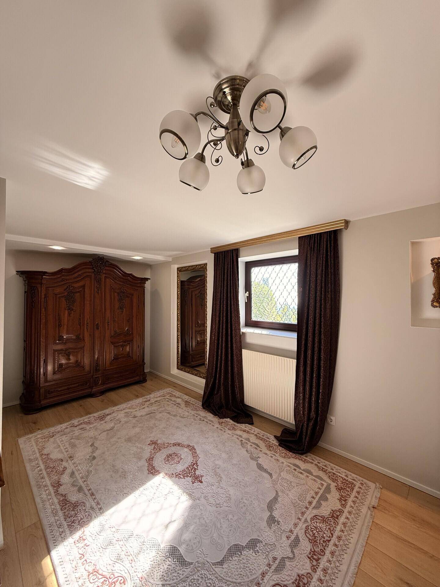Schlafzimmer mit großem Holzschrank, Fenster und traditionellem Teppichboden.