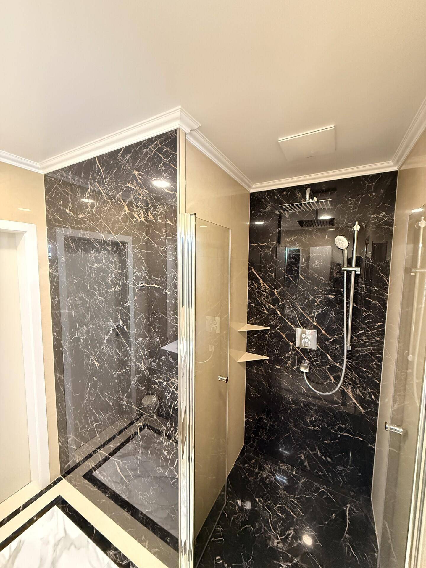 Geräumige Duschkabine mit dunklen Marmorfliesen und moderner Regendusche in einem stilvollen Badezimmer.