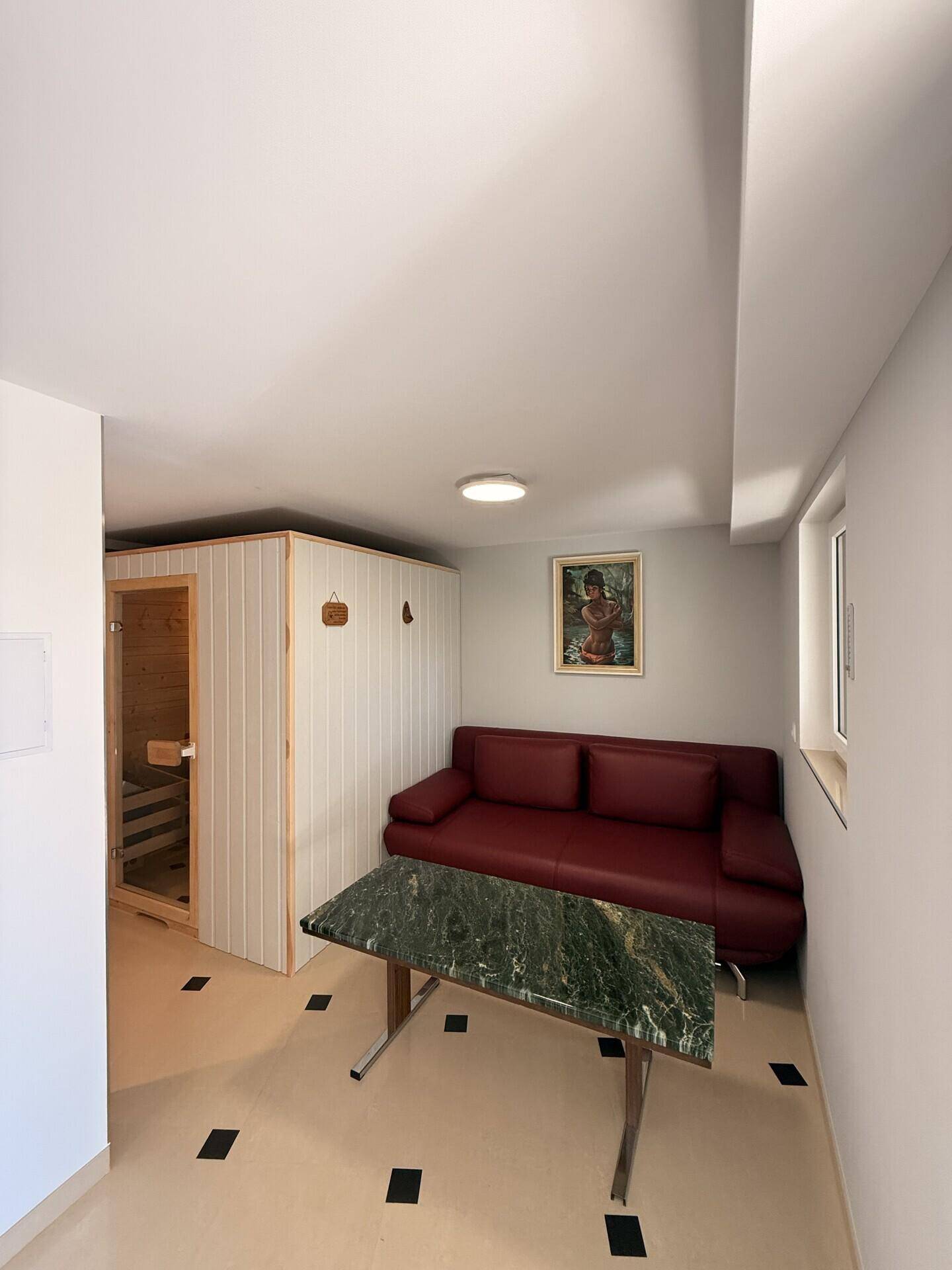 Gemütlicher Wellnessbereich mit Sauna, rotem Sofa und kleinem Tisch.