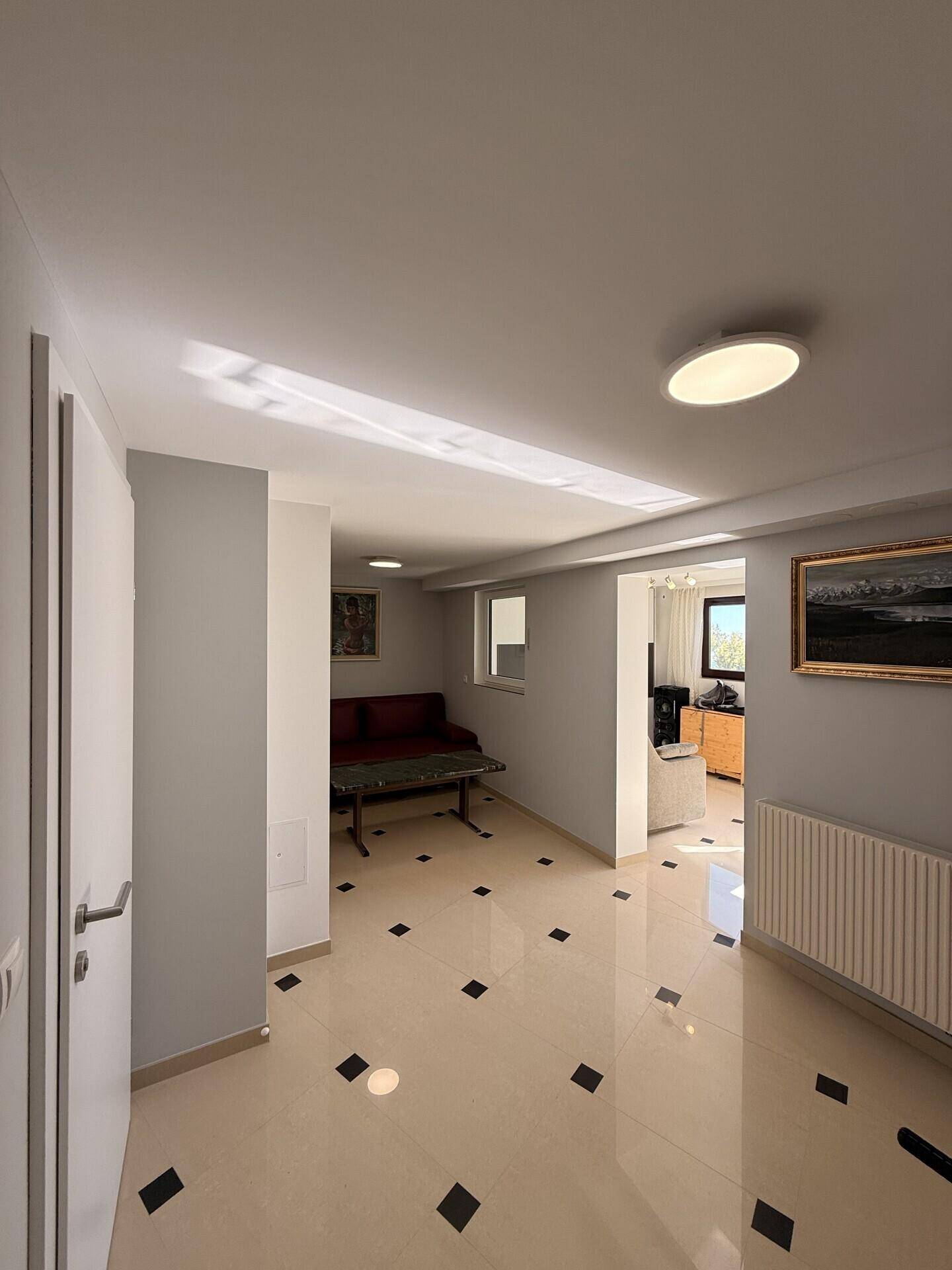 Geräumiger Wohnbereich mit Fliesenboden, Sofa und Blick in einen weiteren Raum.